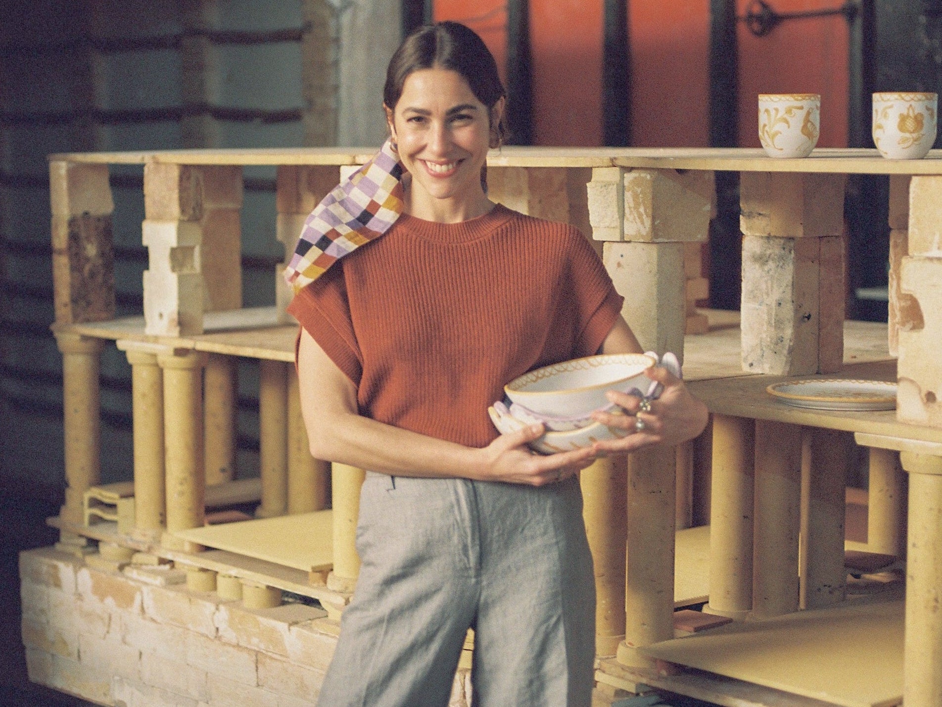 Person holding a bowl in front of a kiln with pottery
