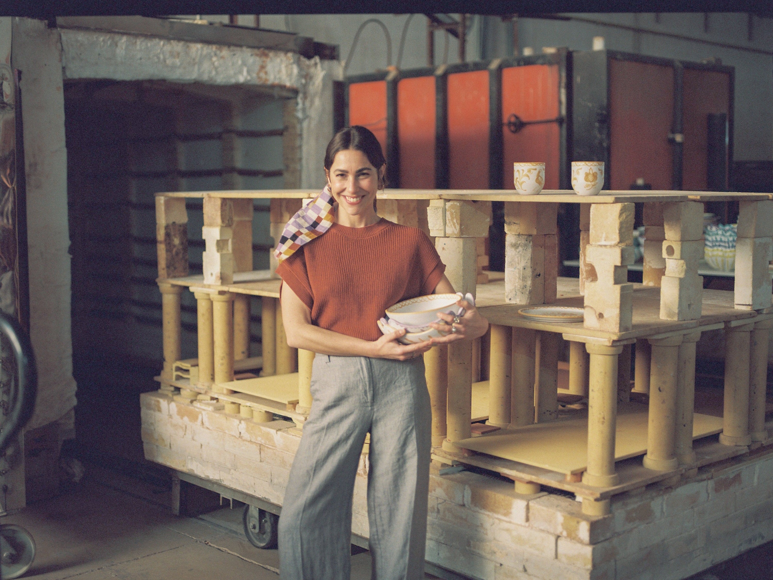 Person holding a bowl in front of a kiln with pottery