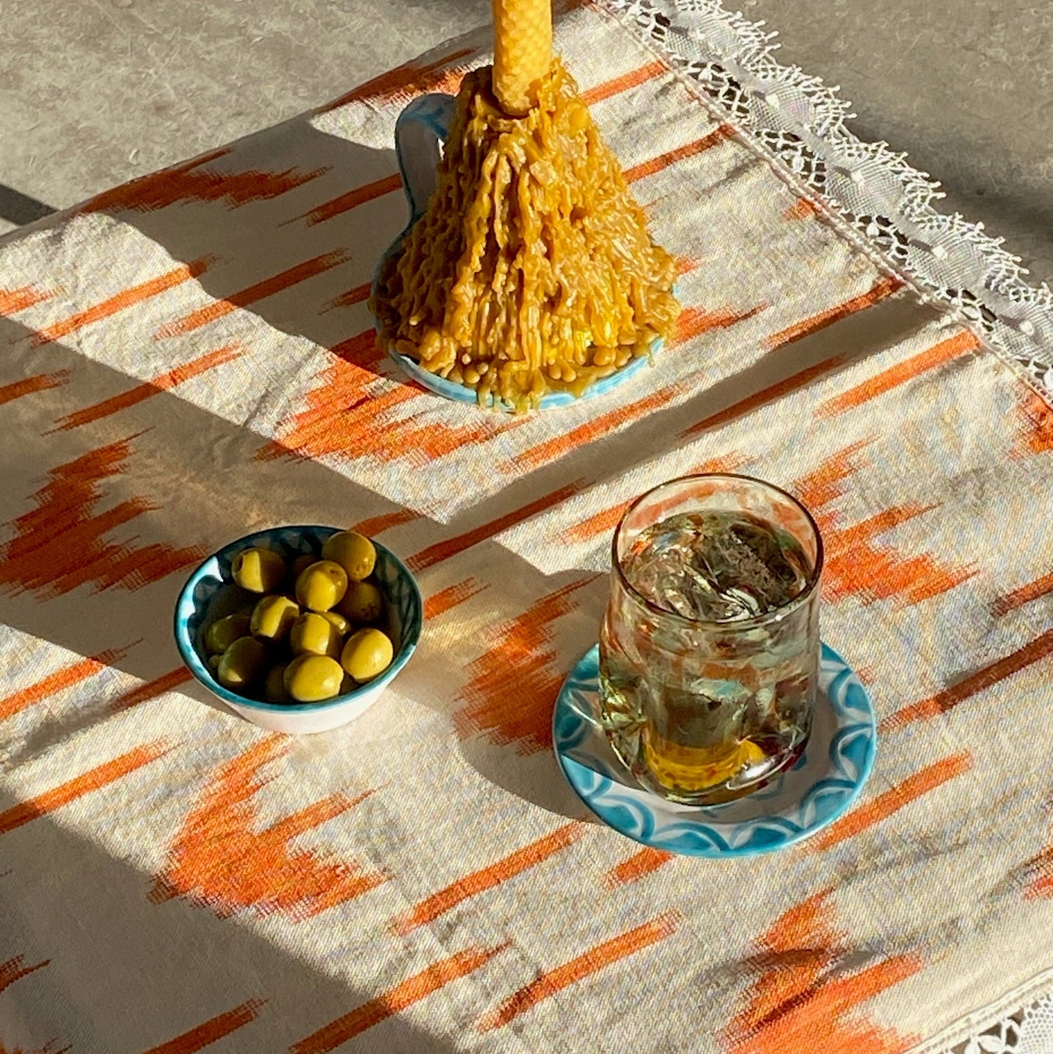 Candle, bowl of olives, and glass with ice on a patterned tablecloth