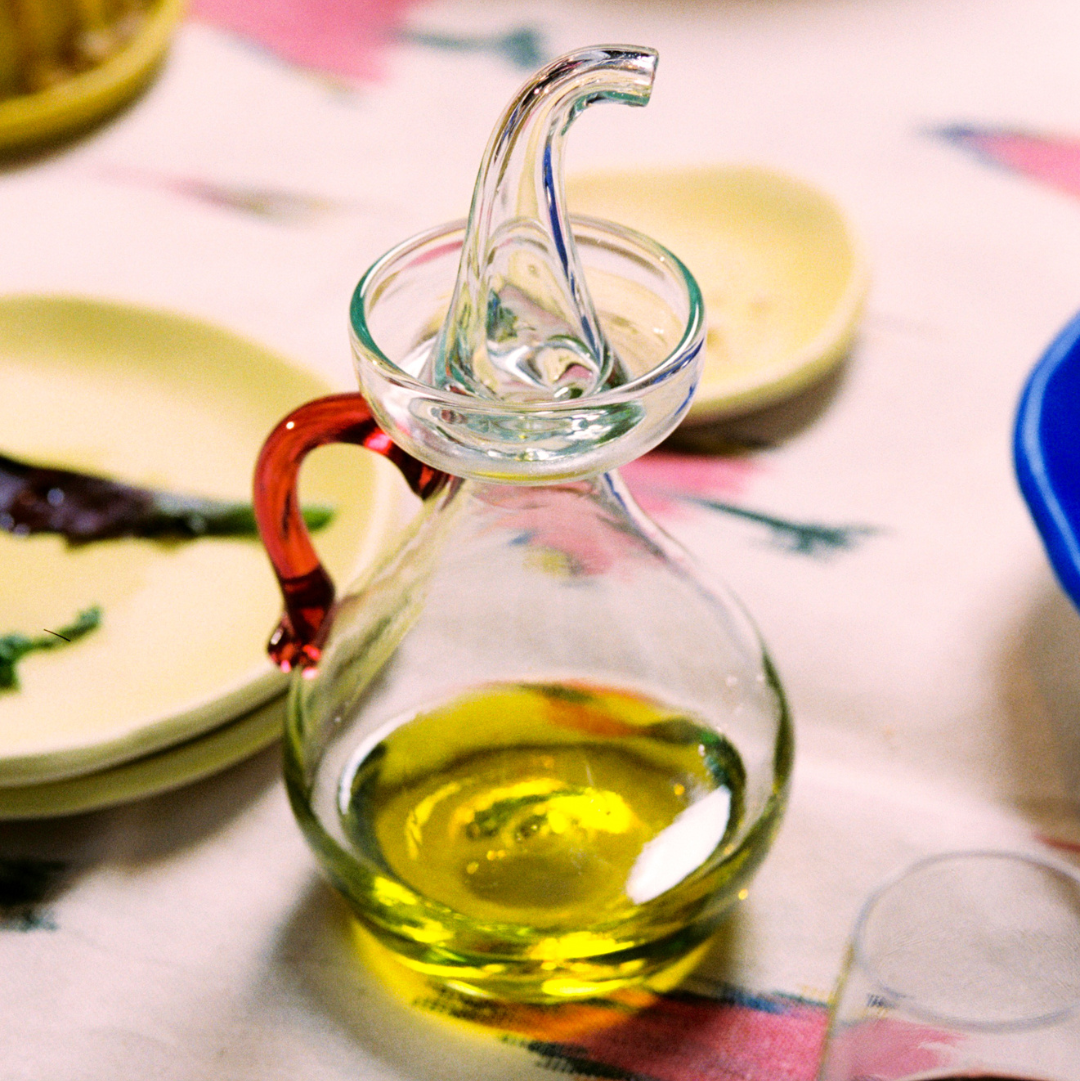  Olive cruet with olive oil on a table with plates in the background