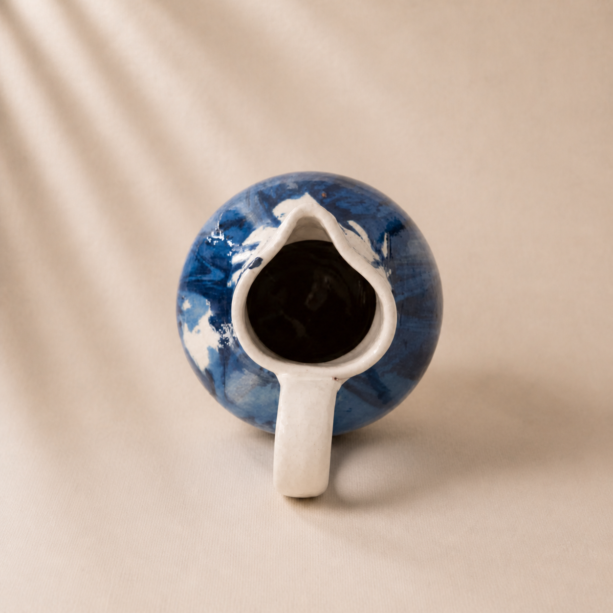 Ceramic pitcher with blue and white marbled design on a beige background
