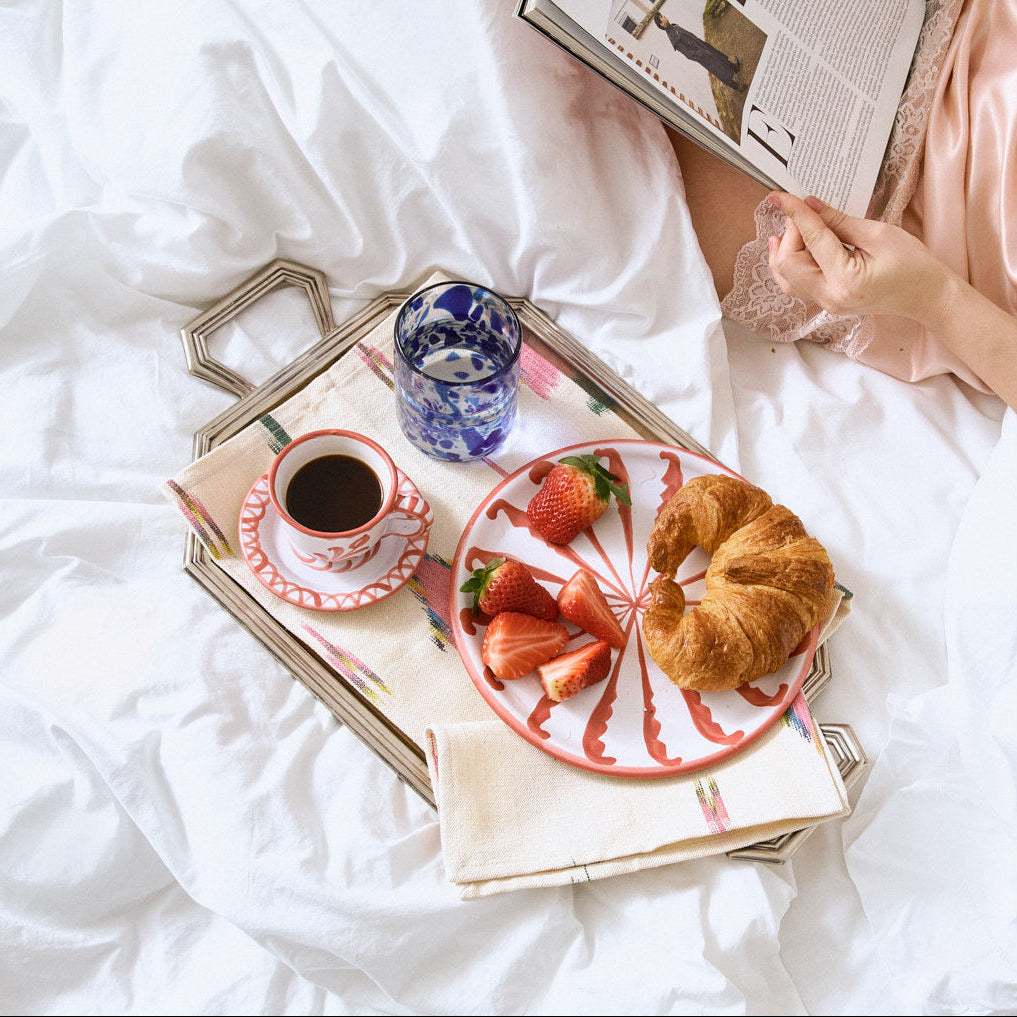 Person lying on a bed with a tray of breakfast food and a newspaper.