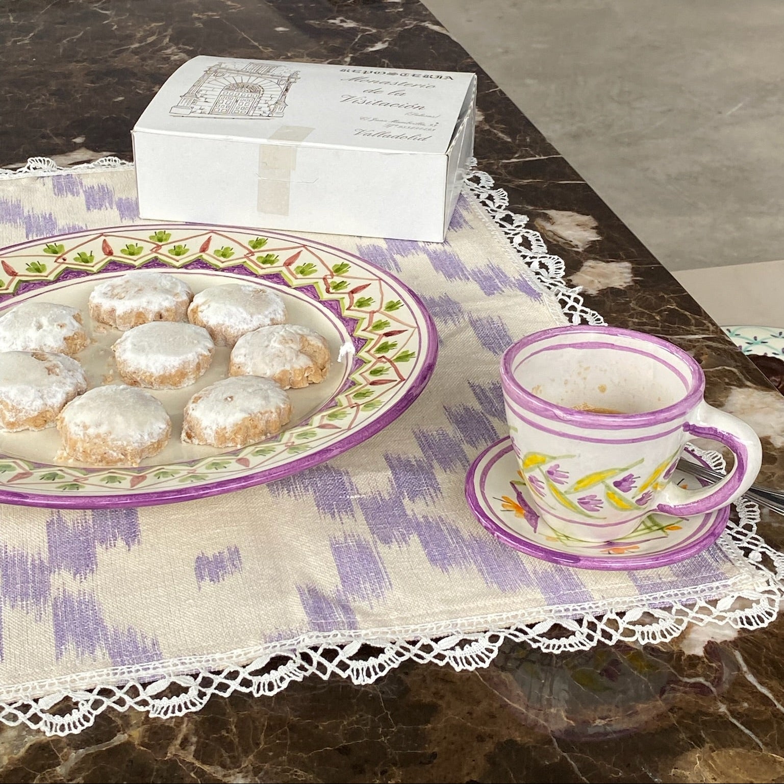 Cookies on a decorative plate with a teacup and saucer on a marble surface