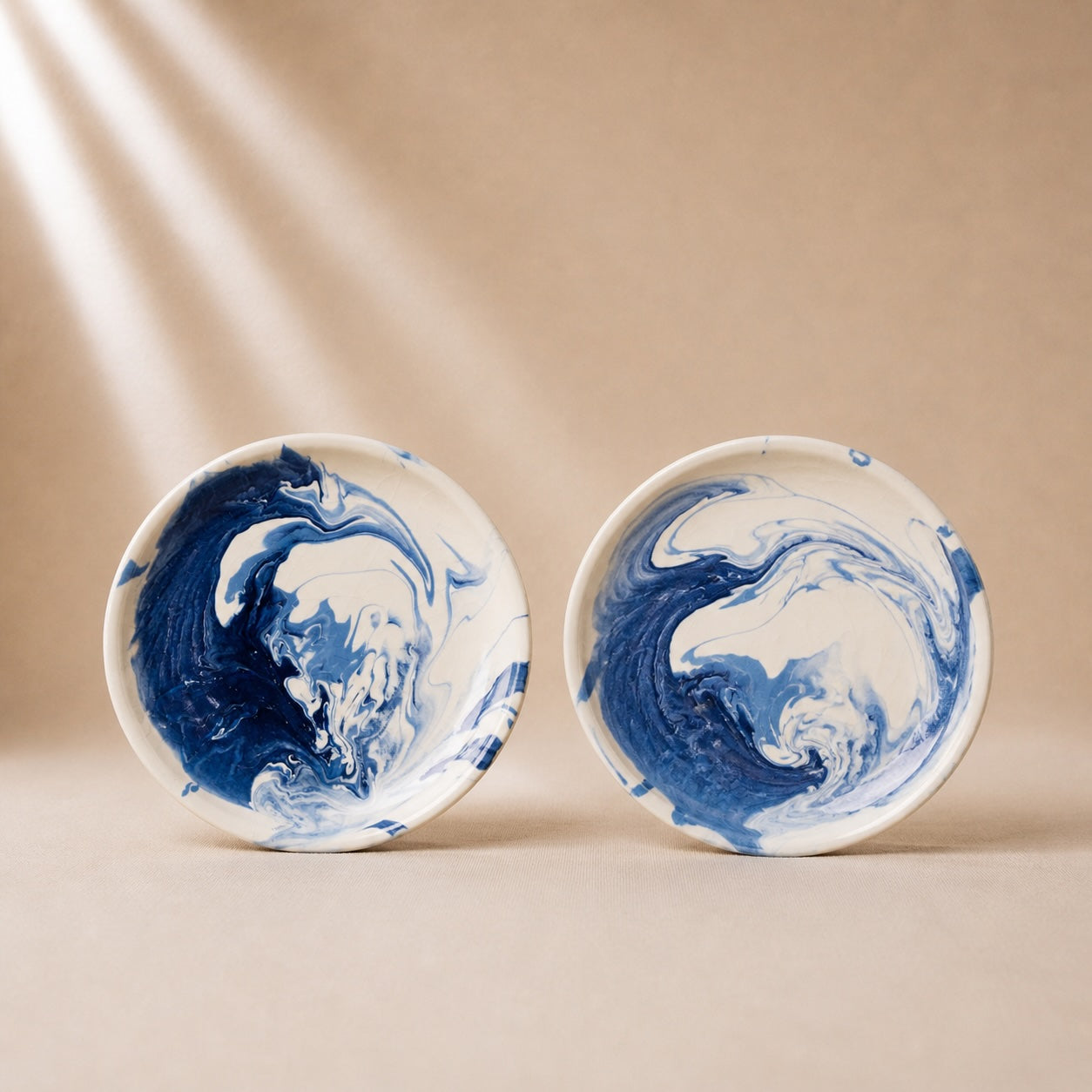 Two ceramic plates with blue and white marbled design on a beige background