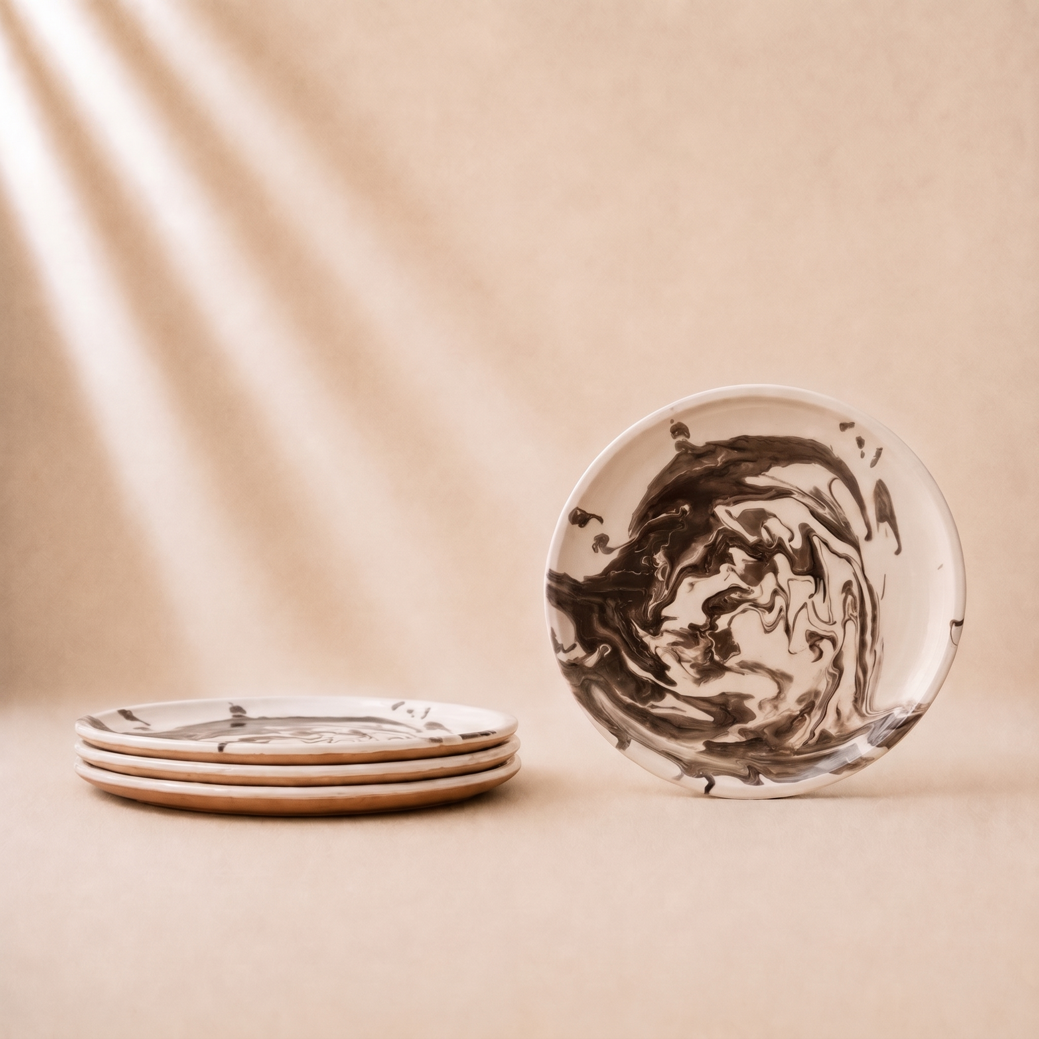 A set of ceramic plates with a dark brown marbled swirl pattern on a warm beige background, with one standing plate and a stack of plates on the left.