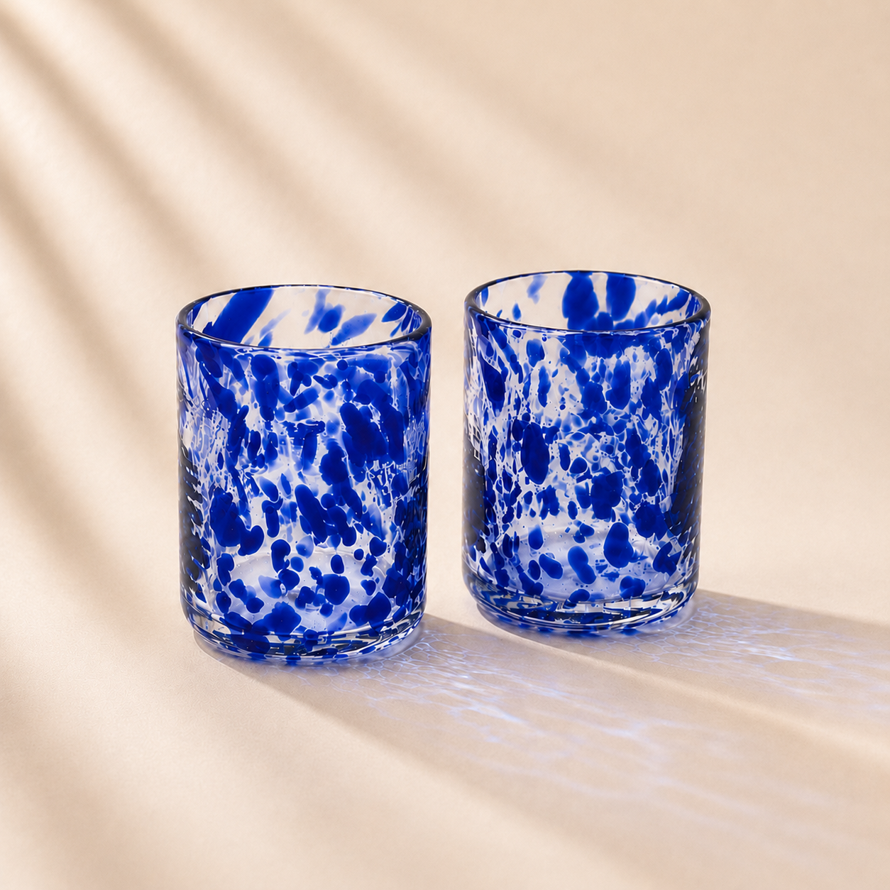 Two blue and white speckled glass tumblers on a beige surface with a soft focus background.