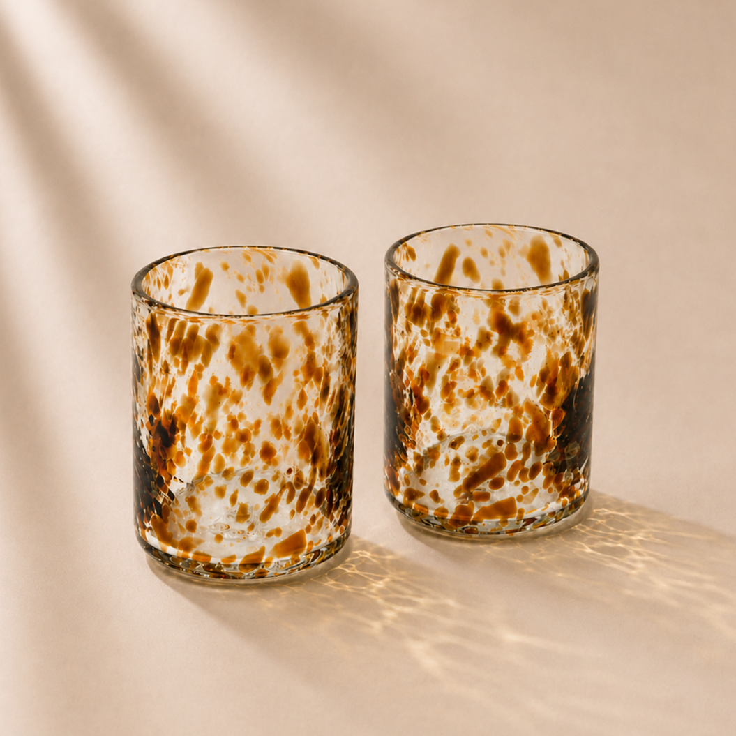 Two glass tumblers with a brown and white speckled pattern on a beige background
