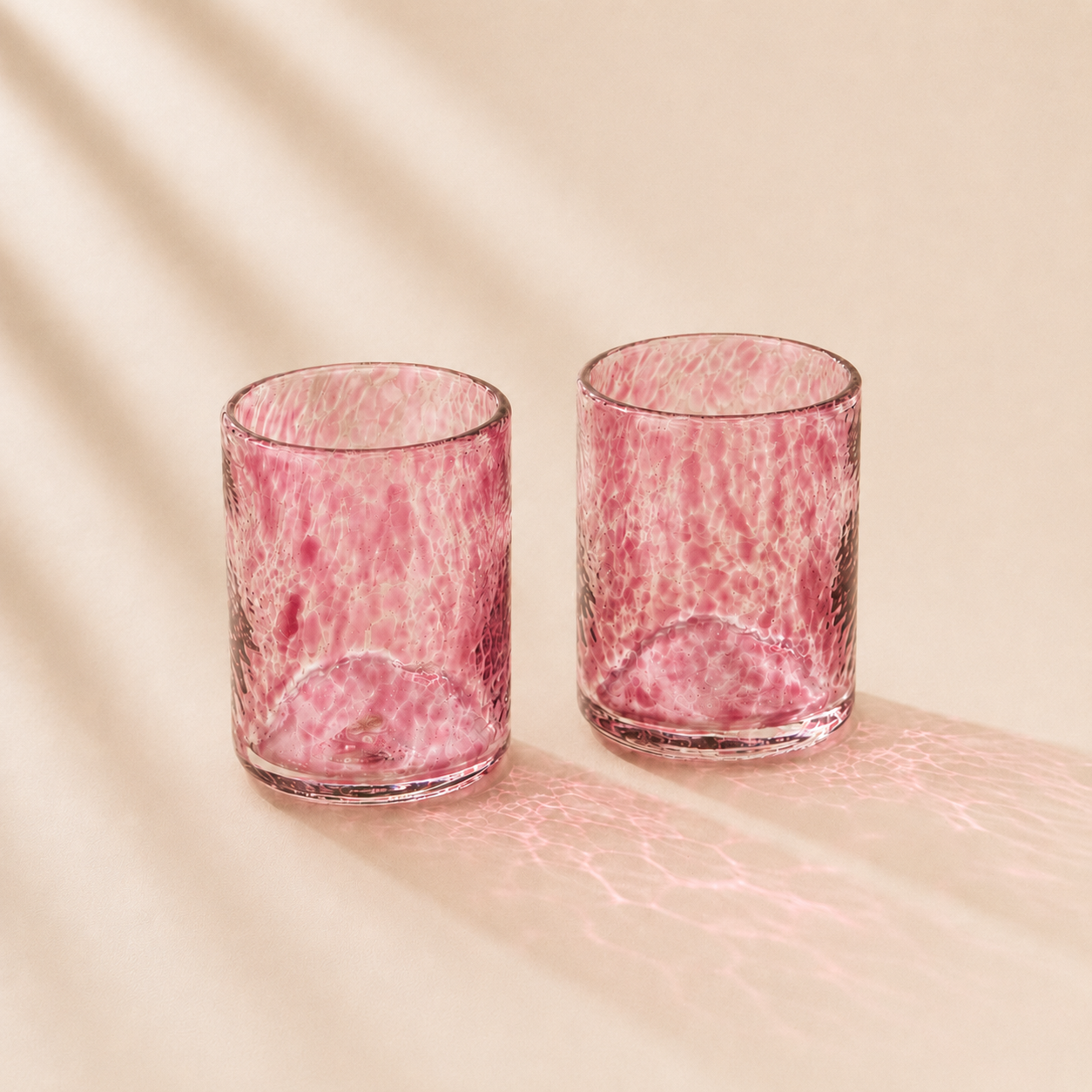 Two pink textured glass tumblers on a beige background