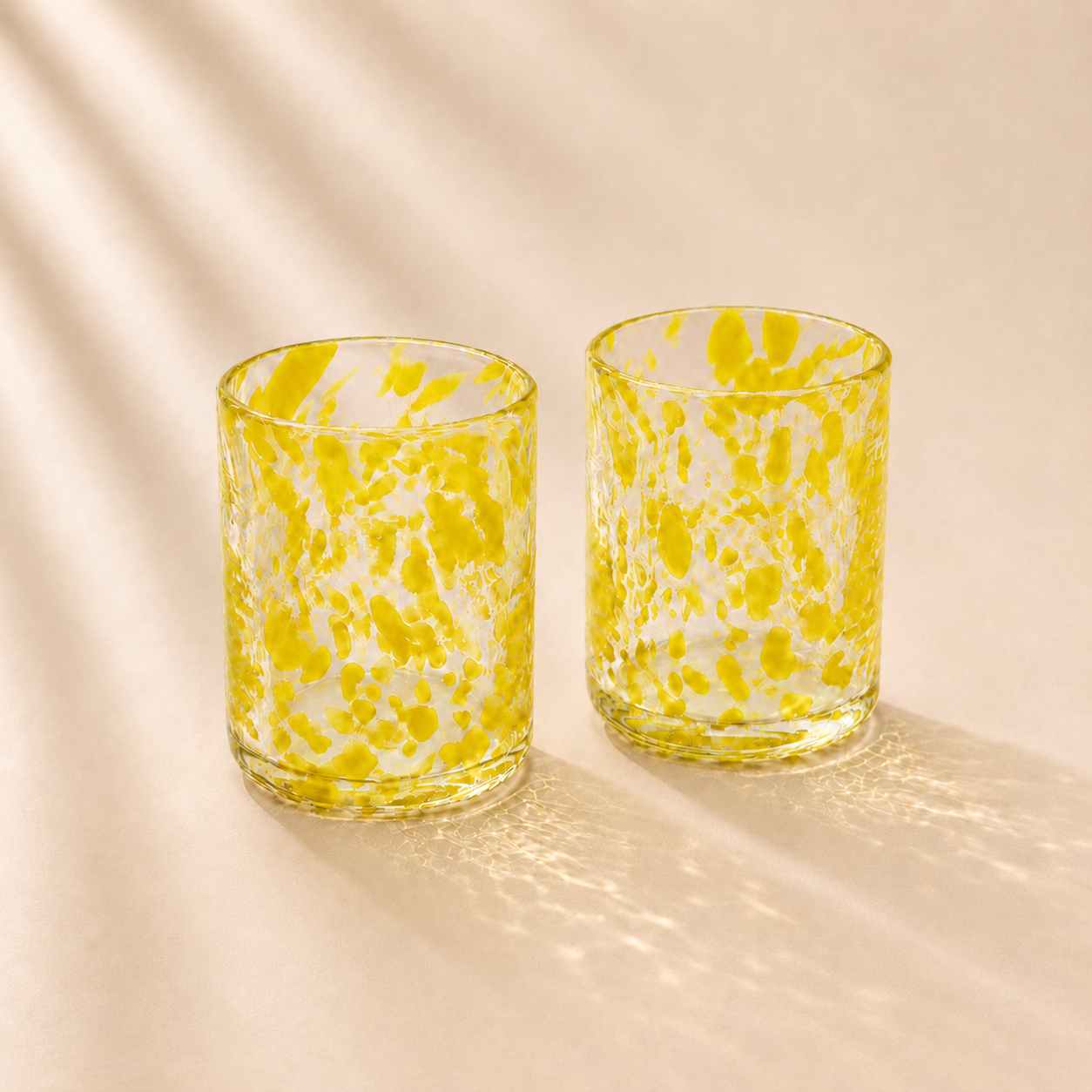 Two yellow and white marbled glass tumblers on a beige background