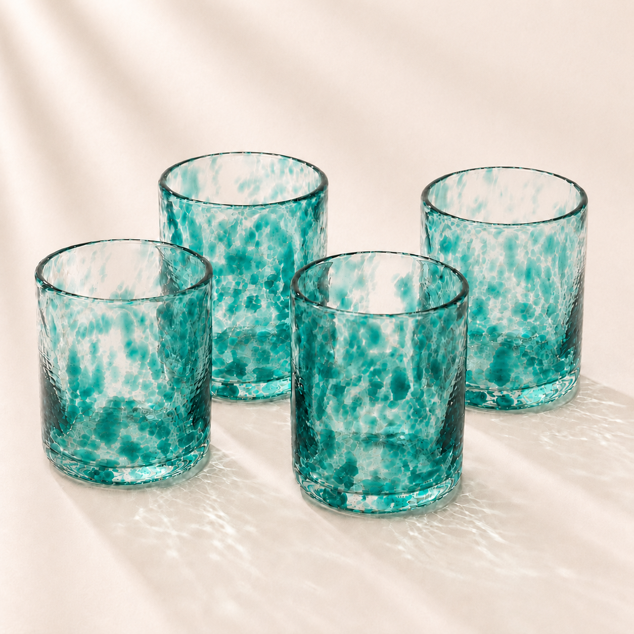 Four teal glass tumblers with a marble-like pattern on a white surface.