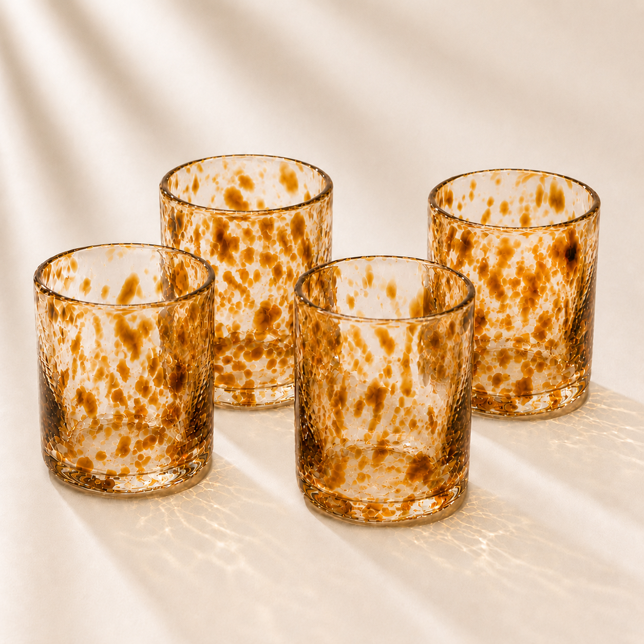 Four glass tumblers with brown speckled pattern on a beige surface