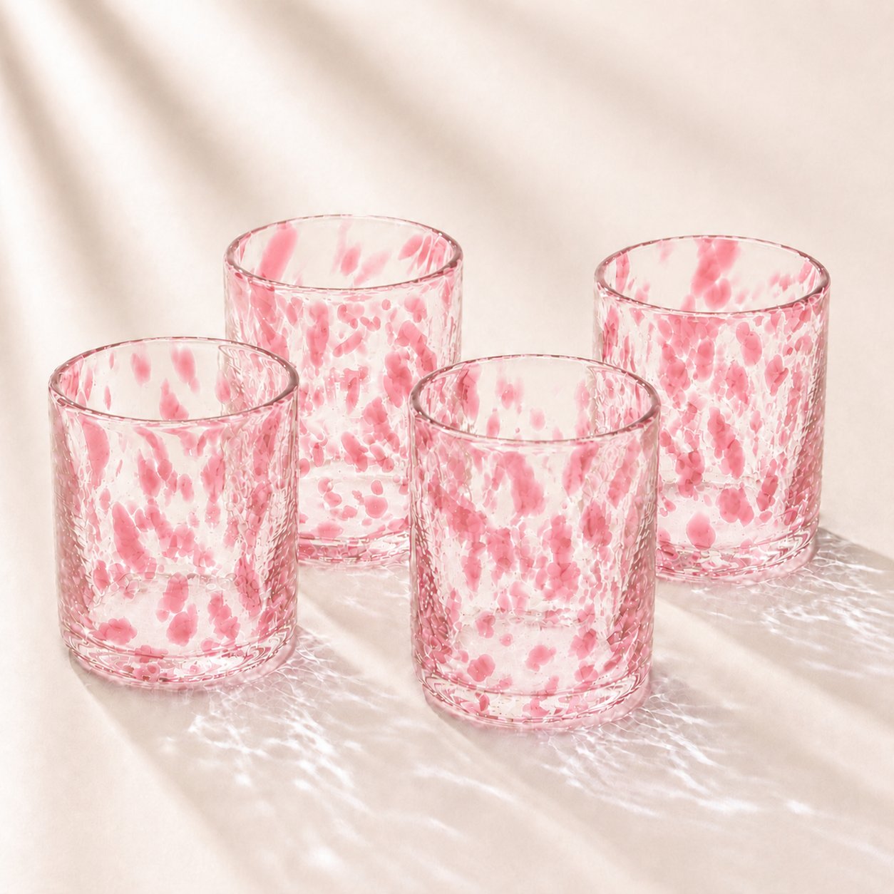 Four pink and clear marbled glass tumblers on a light background