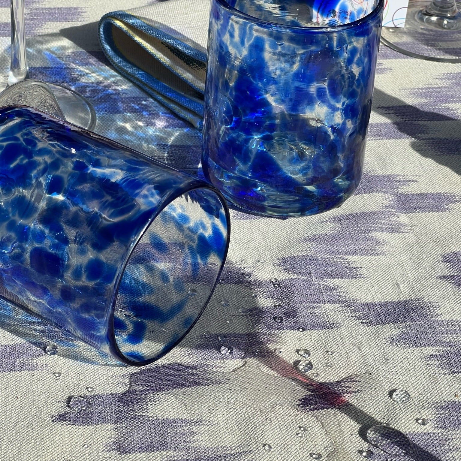 Two blue spotted  glasses tumblers on a patterned tablecloth