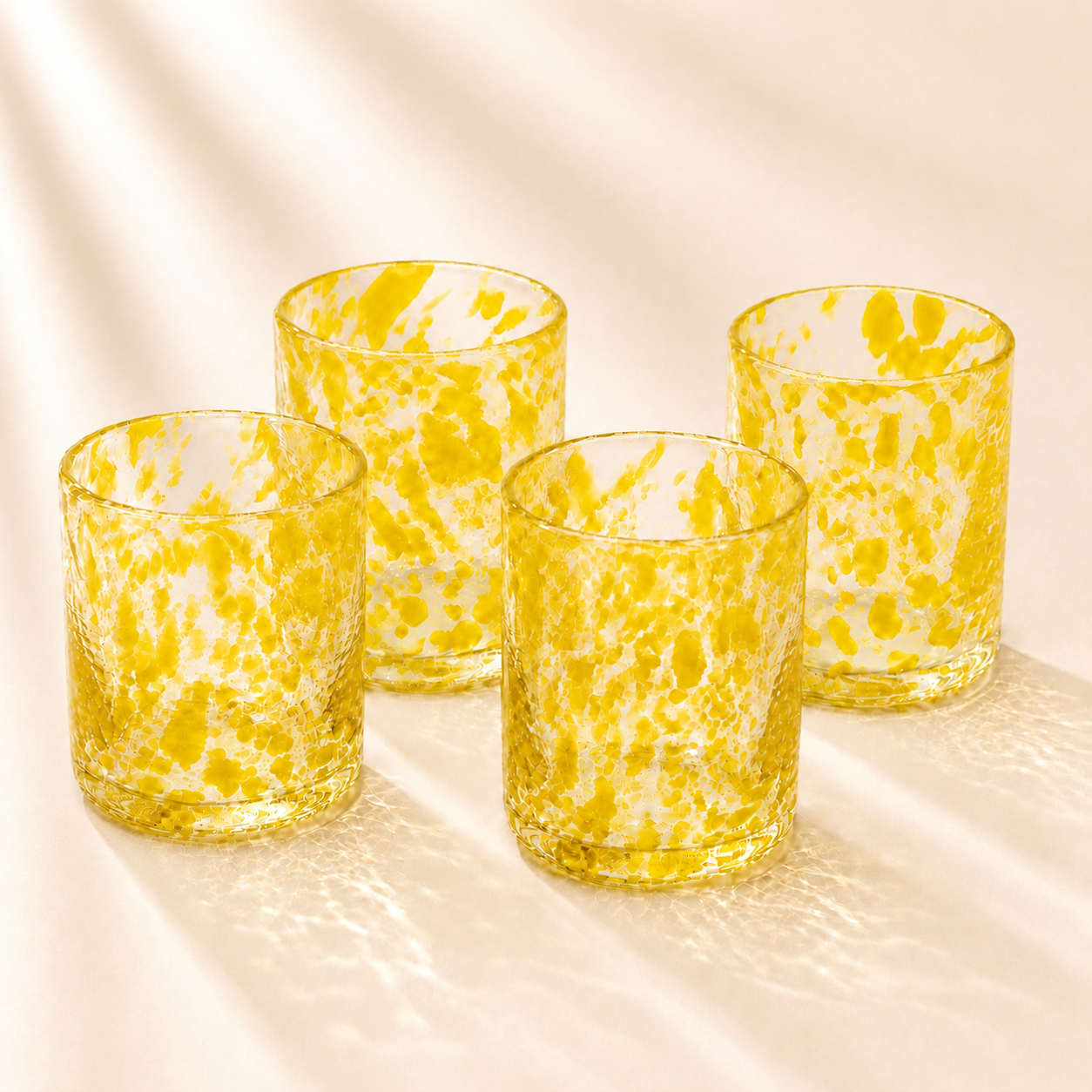 Four yellow spotted  glass tumblers with a marble pattern on a beige surface