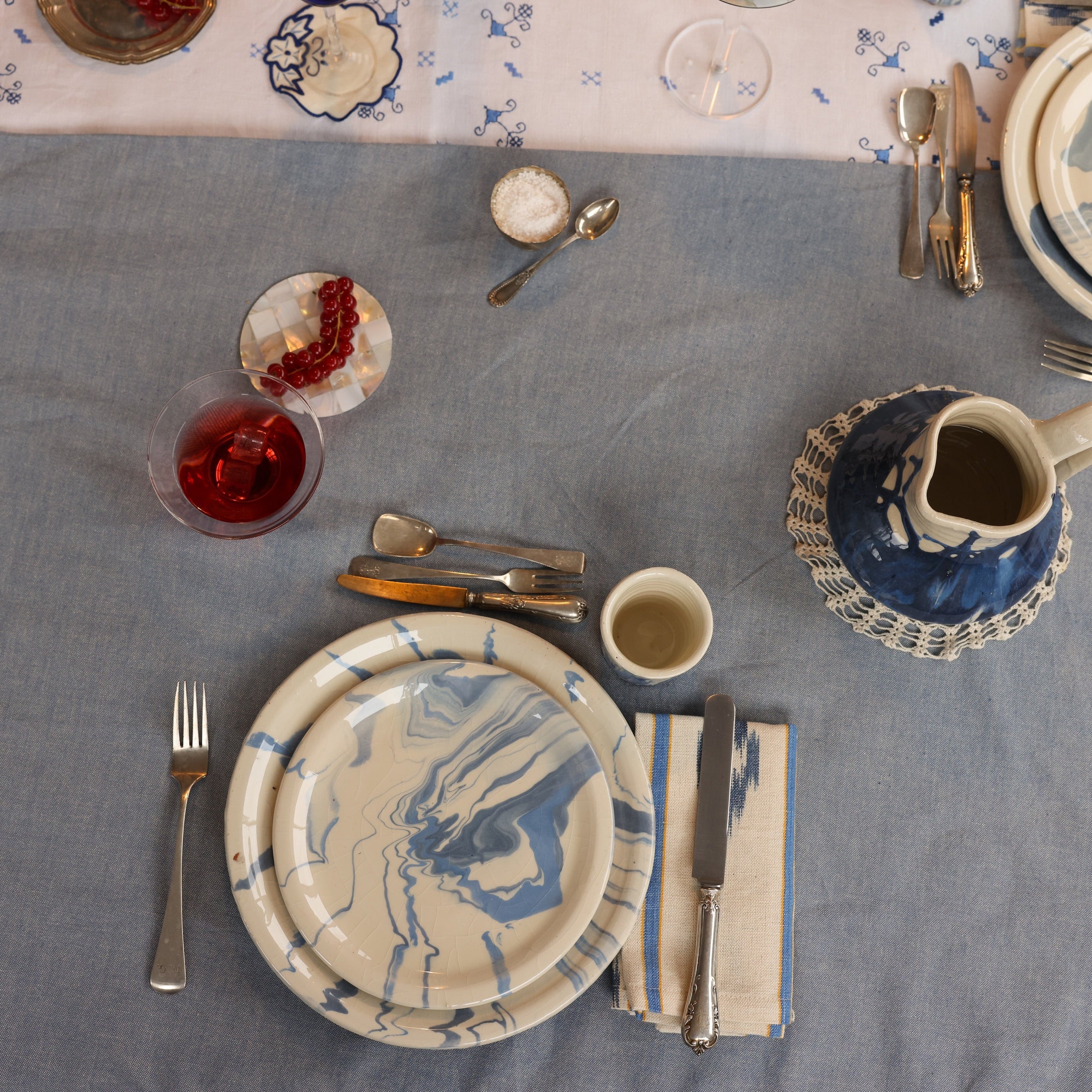 Dining table setting with blue and white ceramic plates, silverware, and a gray tablecloth.