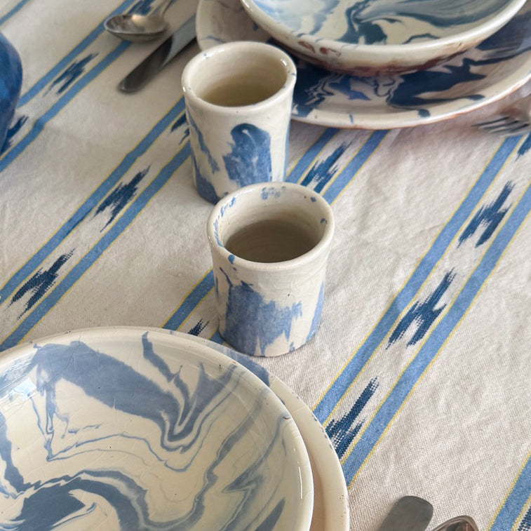 Ceramic cups and plates with blue and white patterns on a striped tablecloth.