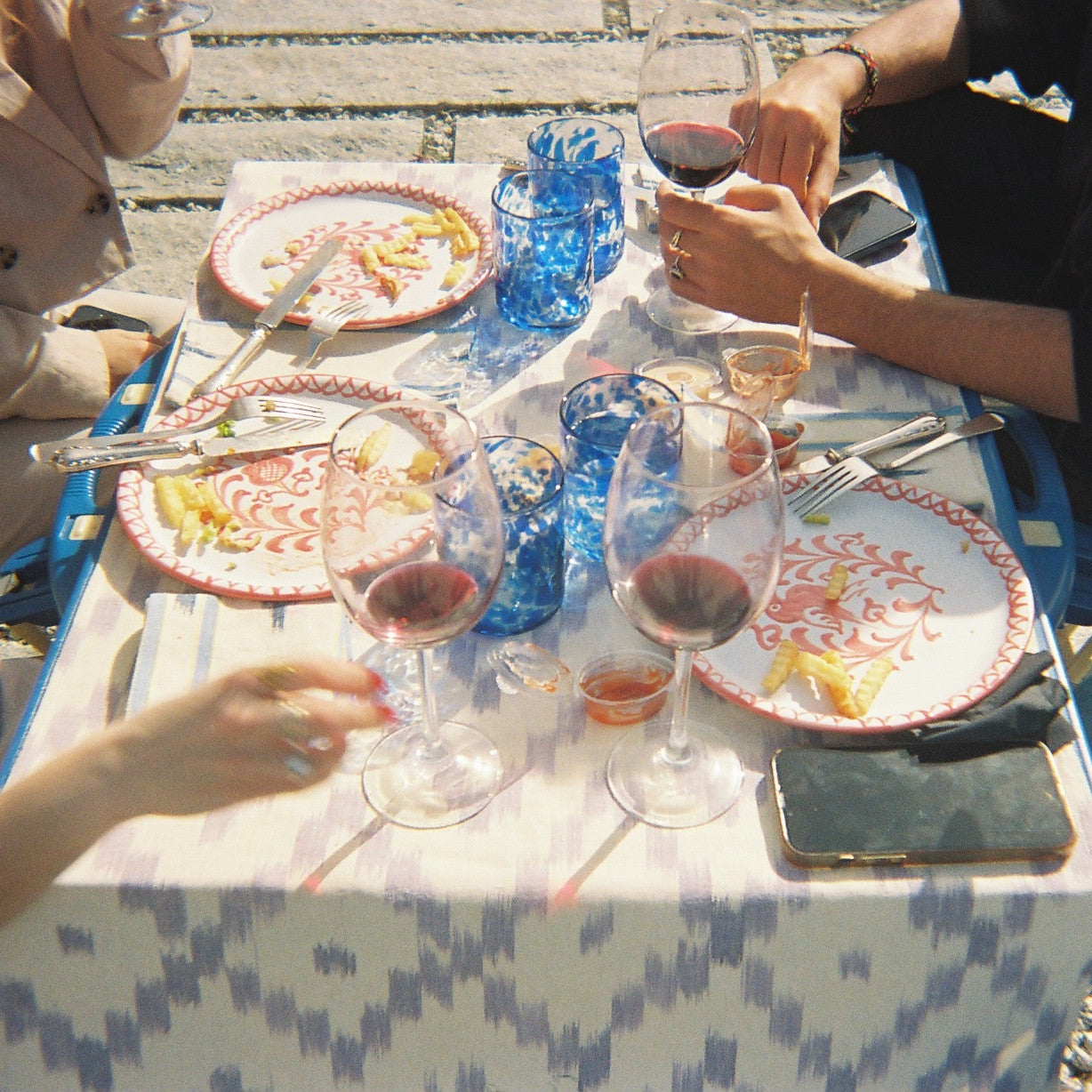 People sitting at a table with wine glasses and plates outdoors on a table runner 