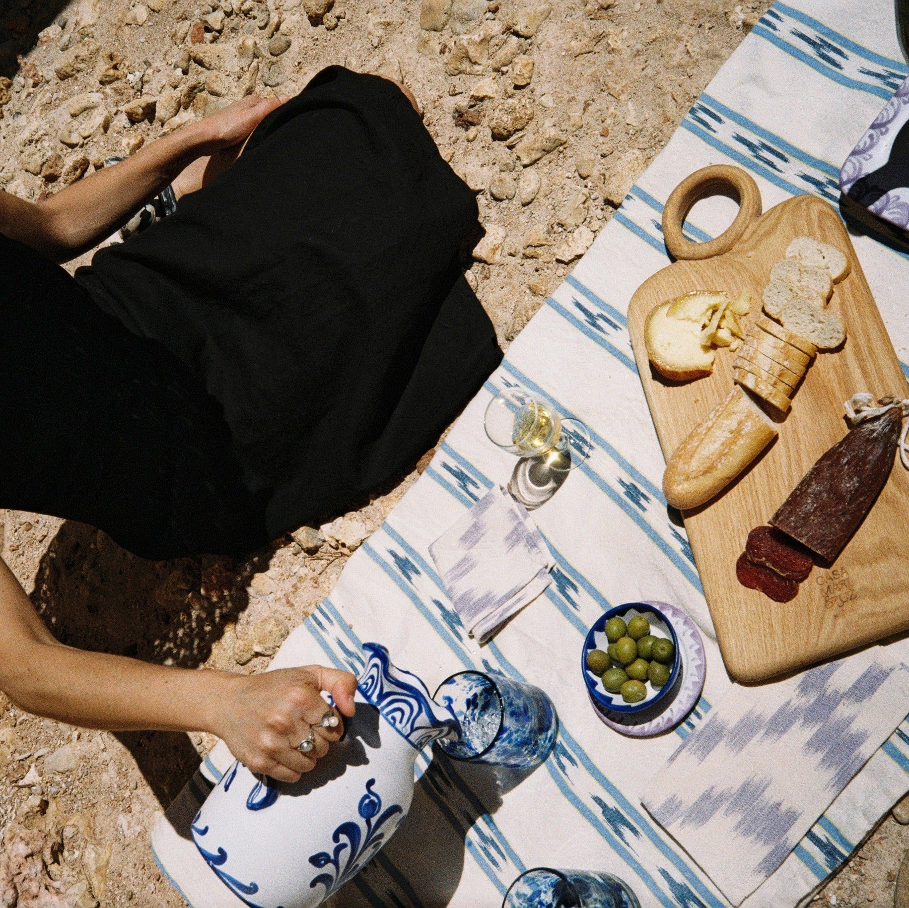 Person sitting on a rocky surface with a picnic setup including table runner, wood board and ceramic