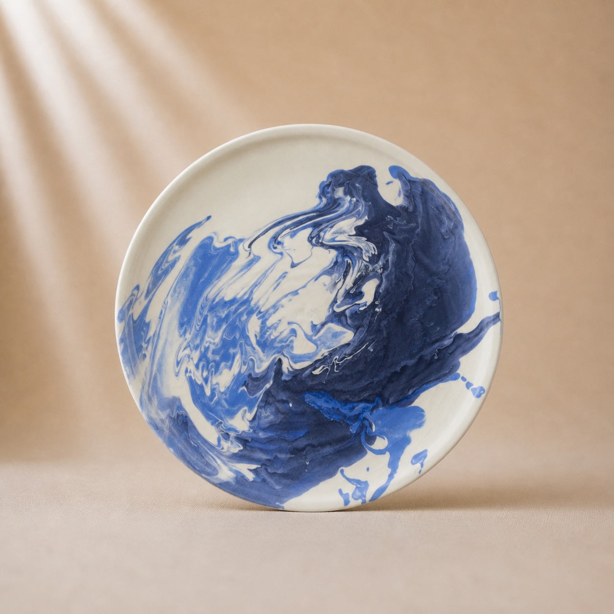 Round ceramic plate with blue and white abstract design on a beige background