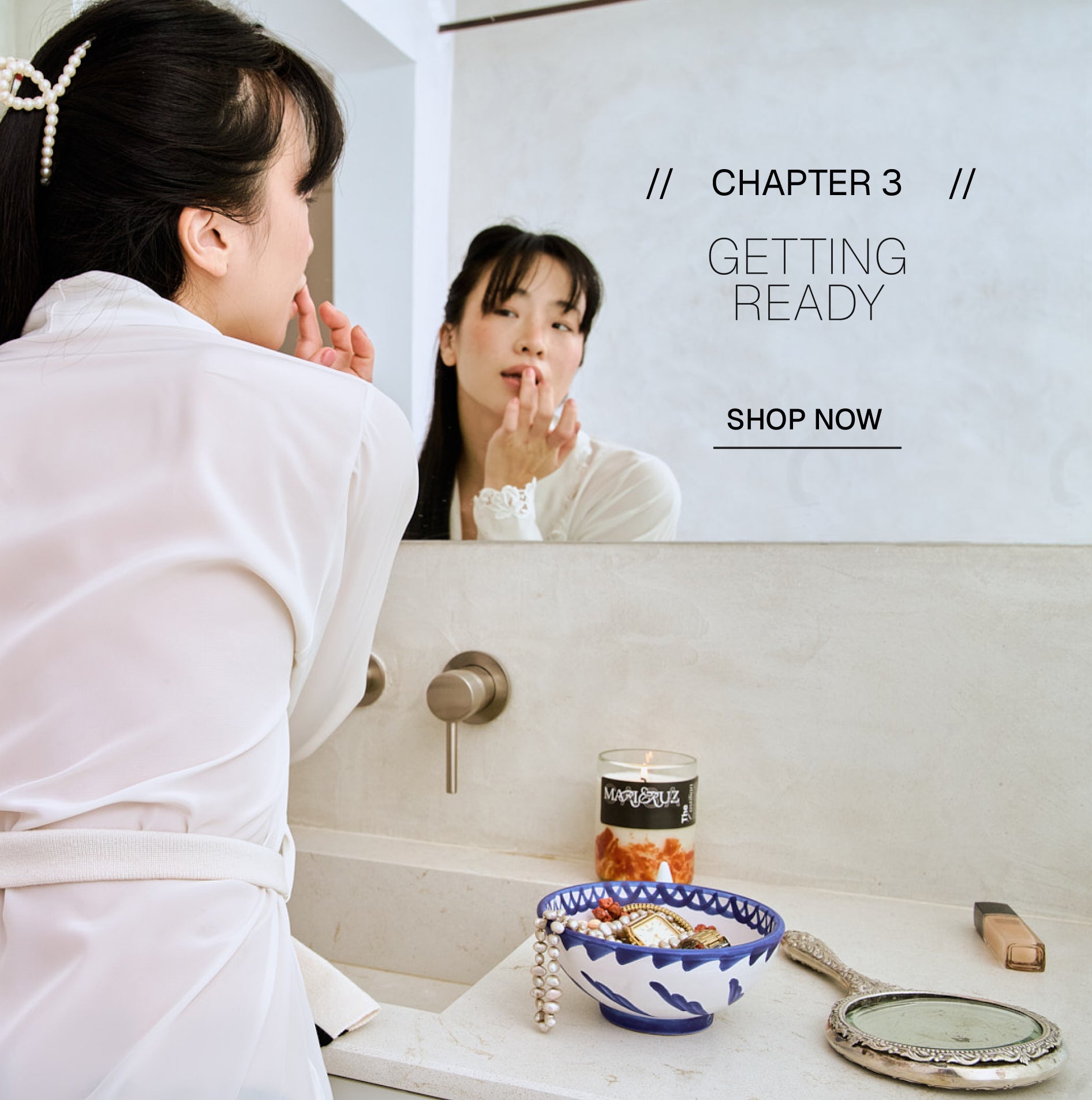 Woman applying makeup in front of a mirror with text 'Chapter 3 Getting Ready Shop Now'.