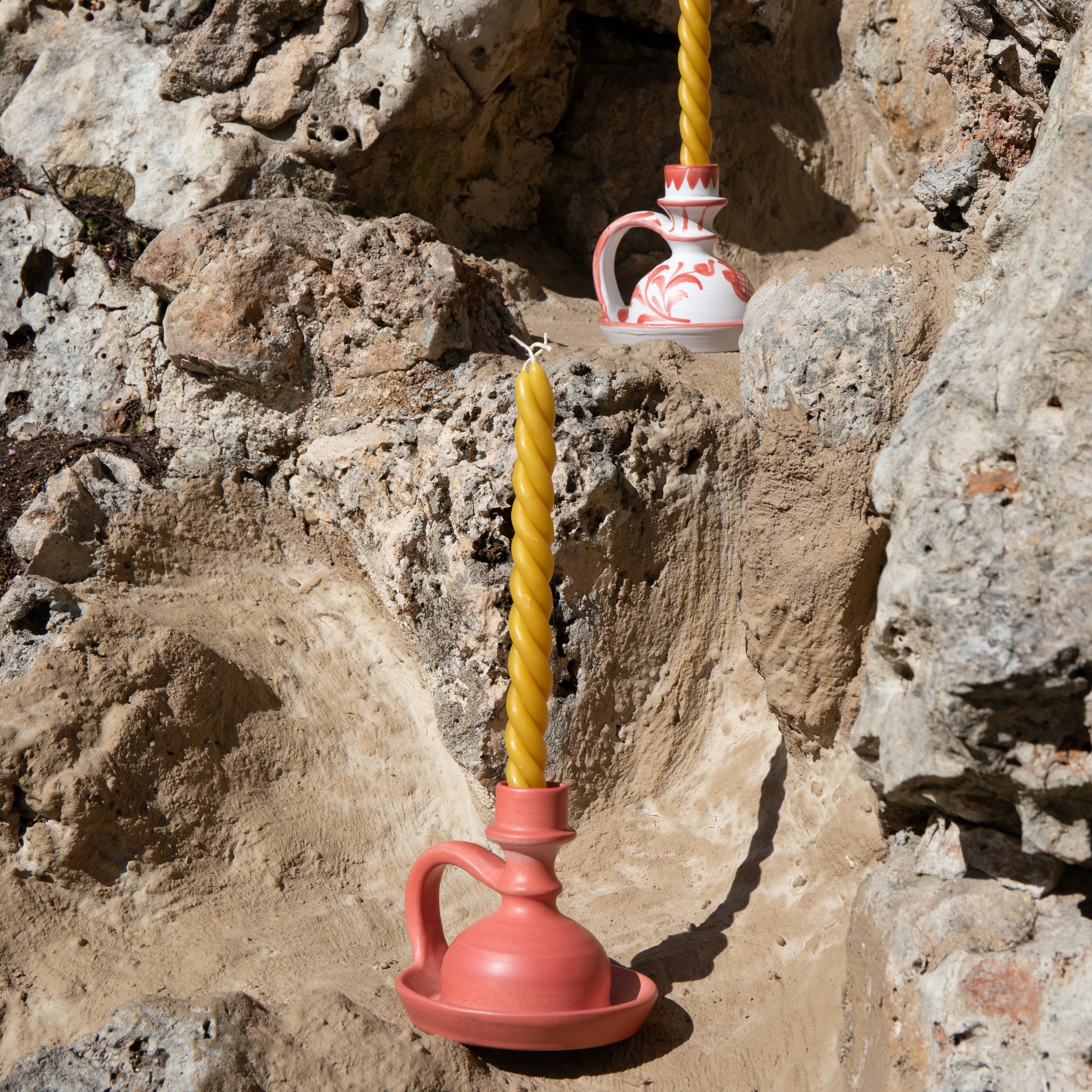 Pink and white ceramic vessels with yellow candles against a rocky background