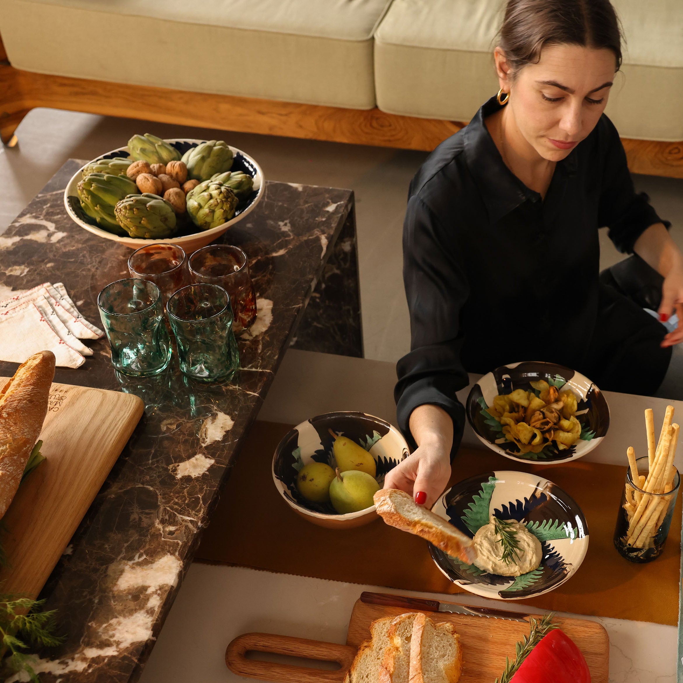 Woman sitting at a table with food and a dog in a cozy living room.
