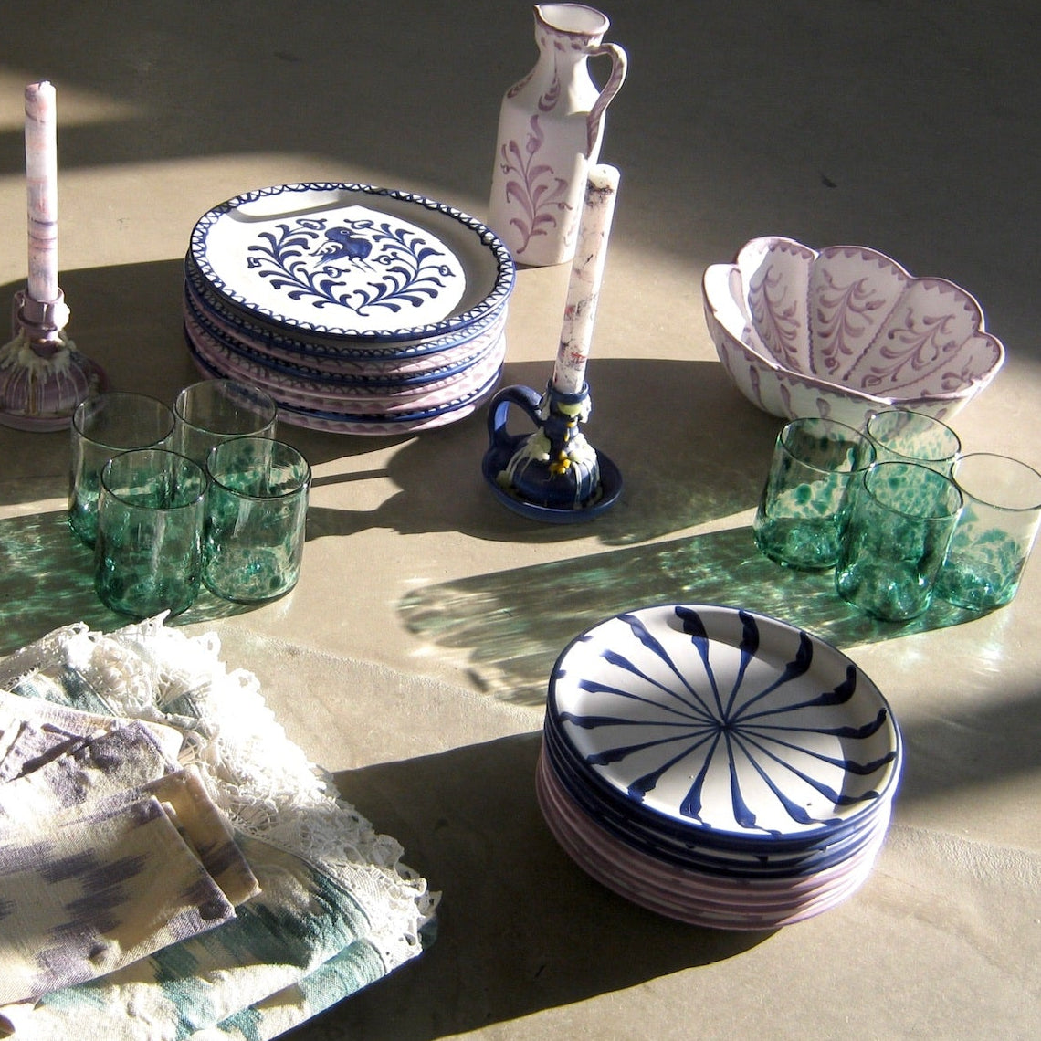 Ceramic plates with blue patterns on a table with green glasses and decorative items. - lifestyle