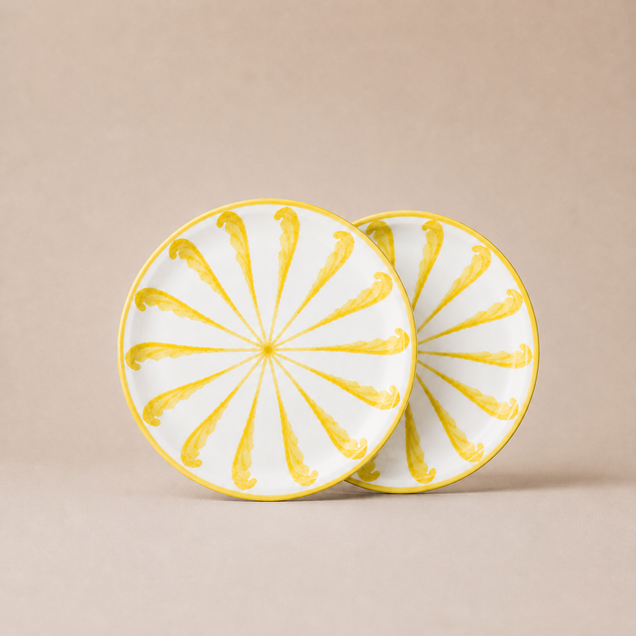 Two ceramic plates with yellow sunburst design on a beige background