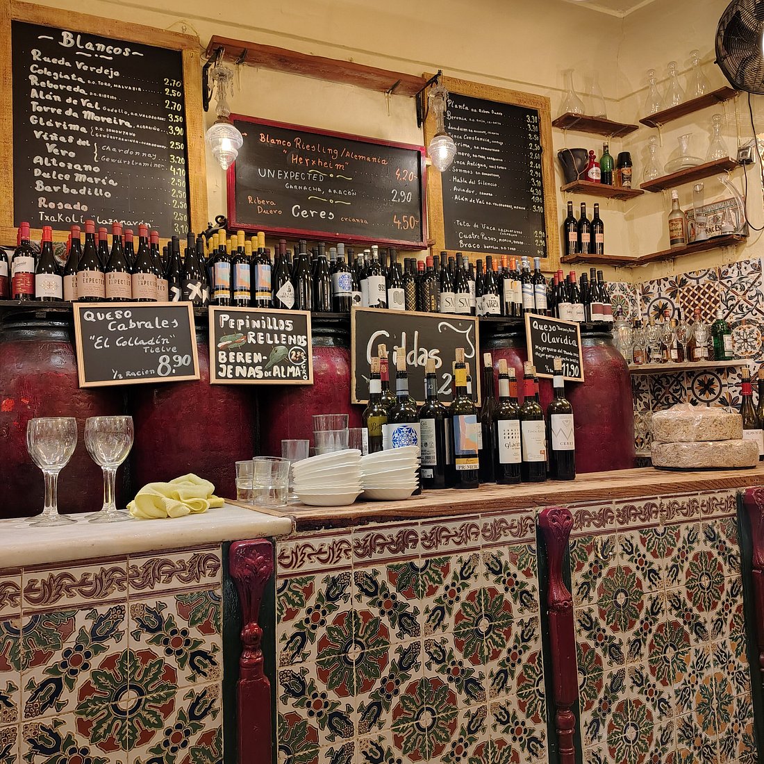 Barra con botellas de vino, copas y una pizarra de menú en un entorno rústico.