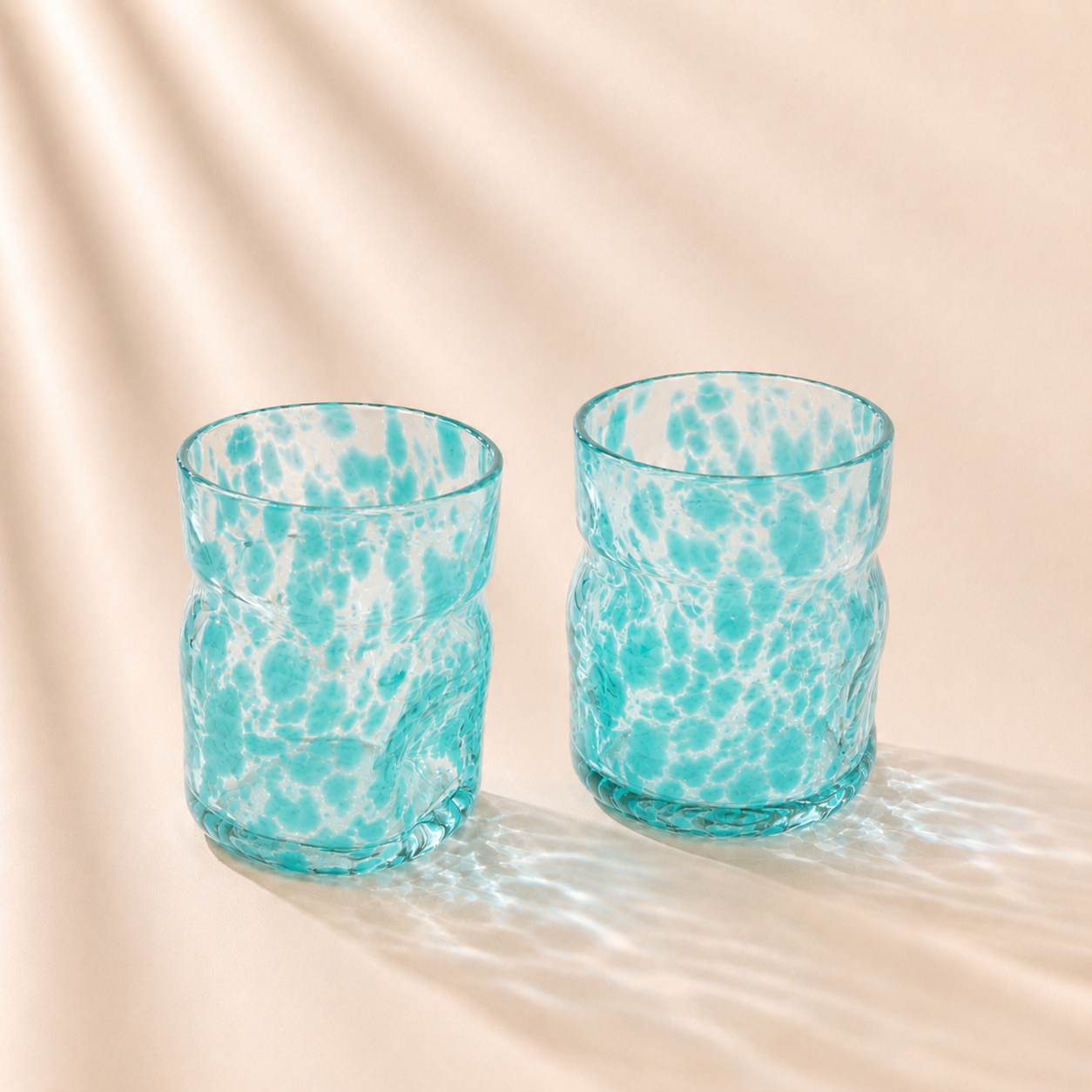 Two turquoise glass tumblers with a marbled pattern on a beige background