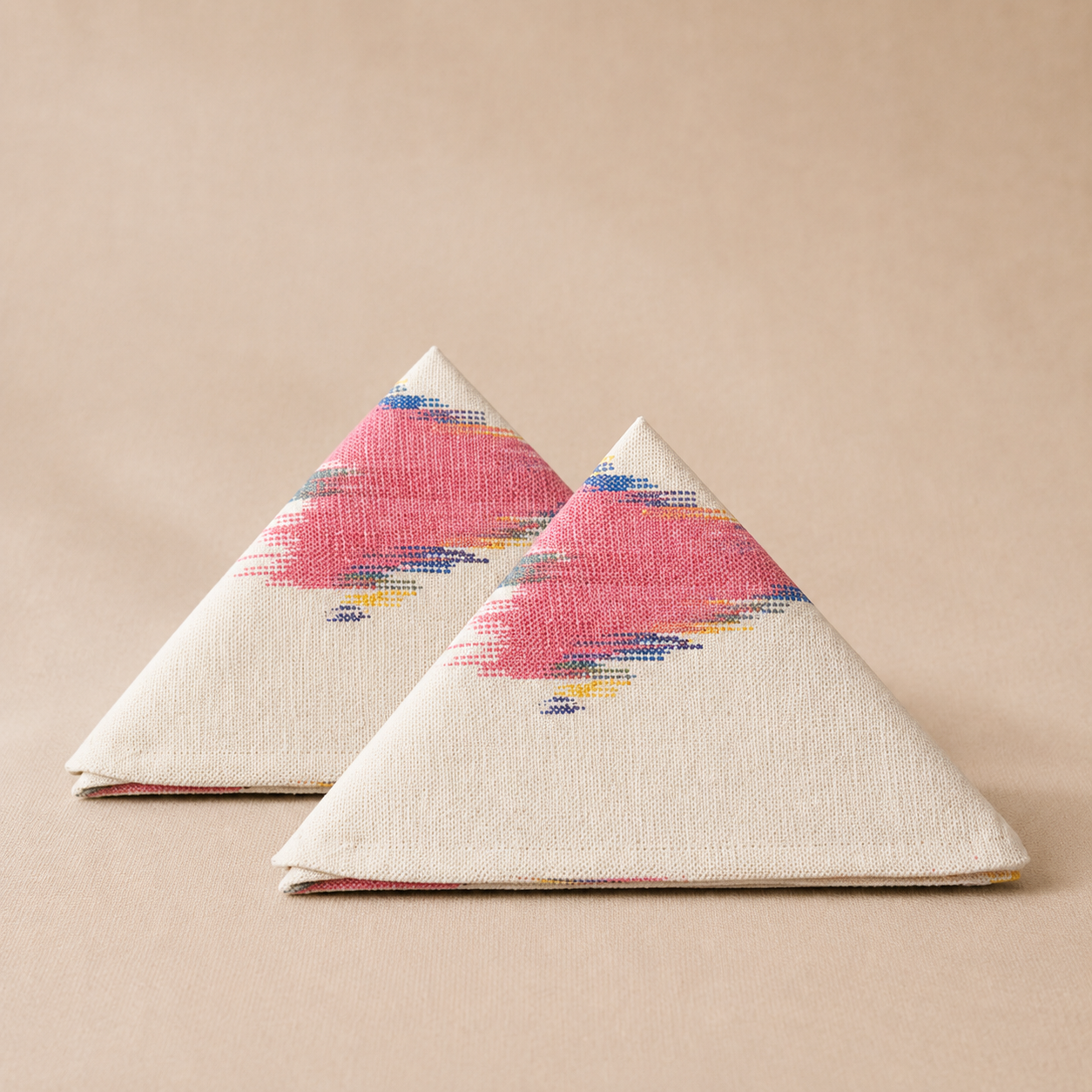 Two triangular napkins with pink and blue abstract patterns on a beige background