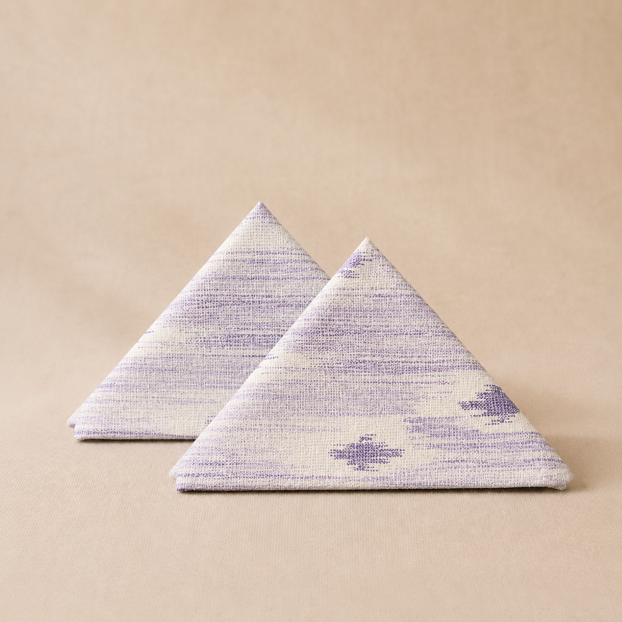 Two triangular napkins with a purple and white pattern on a beige background