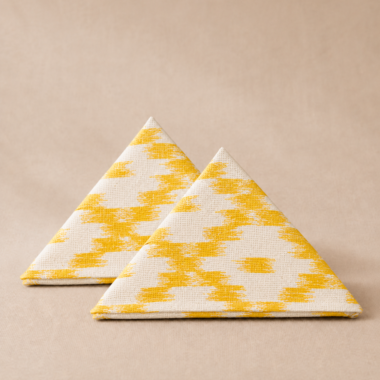 Two triangular napkins with yellow and white pattern on a beige background