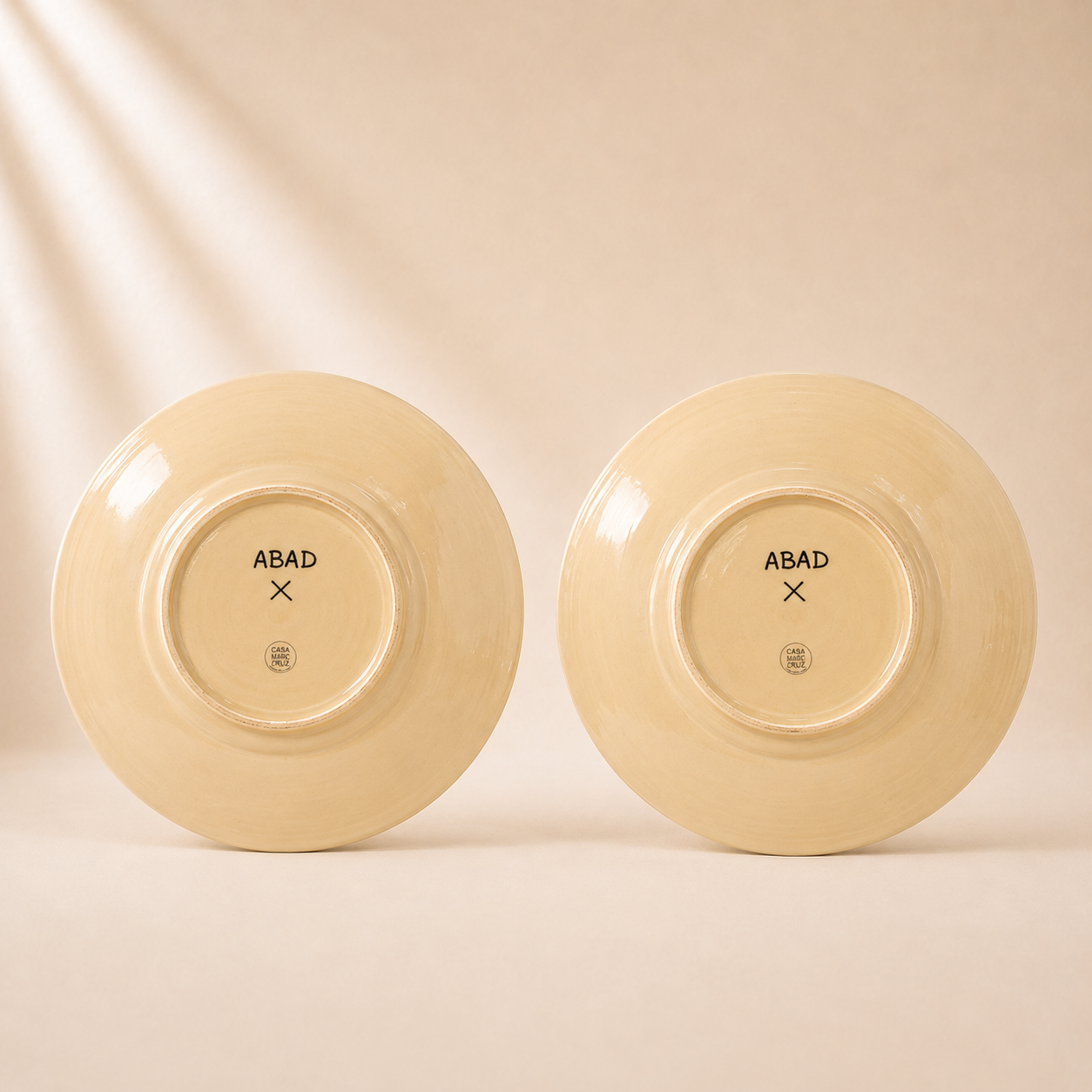 Two beige ceramic plates with 'ABAD' branding on a beige background