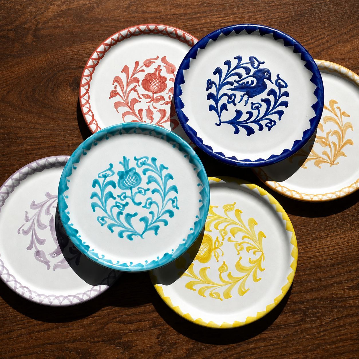 Six decorative ceramic plates with scalloped rims and colorful floral and bird motifs, arranged on a dark wooden surface. - lifestyle
