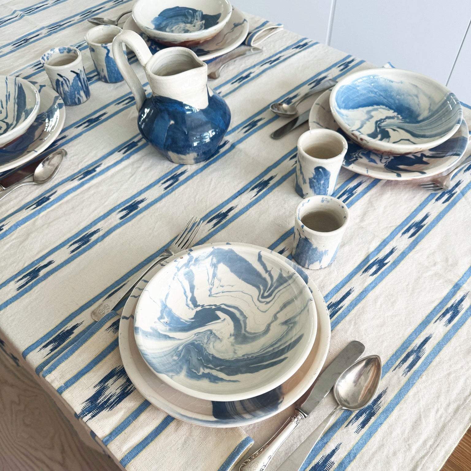 Dining table setting with blue and white marbled plates, cups, and a pitcher on a striped tablecloth -lifestyle