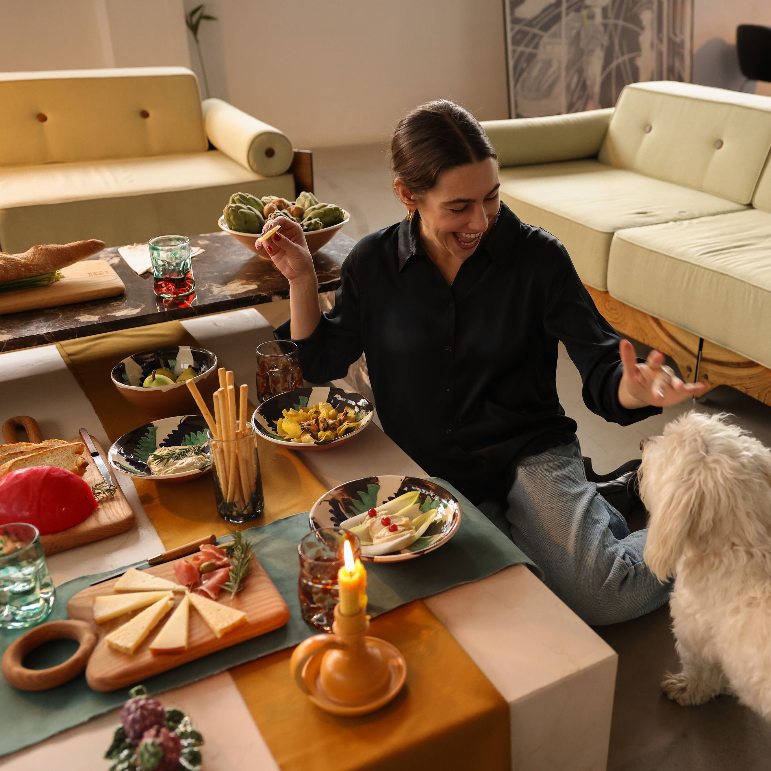 Woman sitting on the floor with a dog in a living room, surrounded by food and drinks -lifestyle