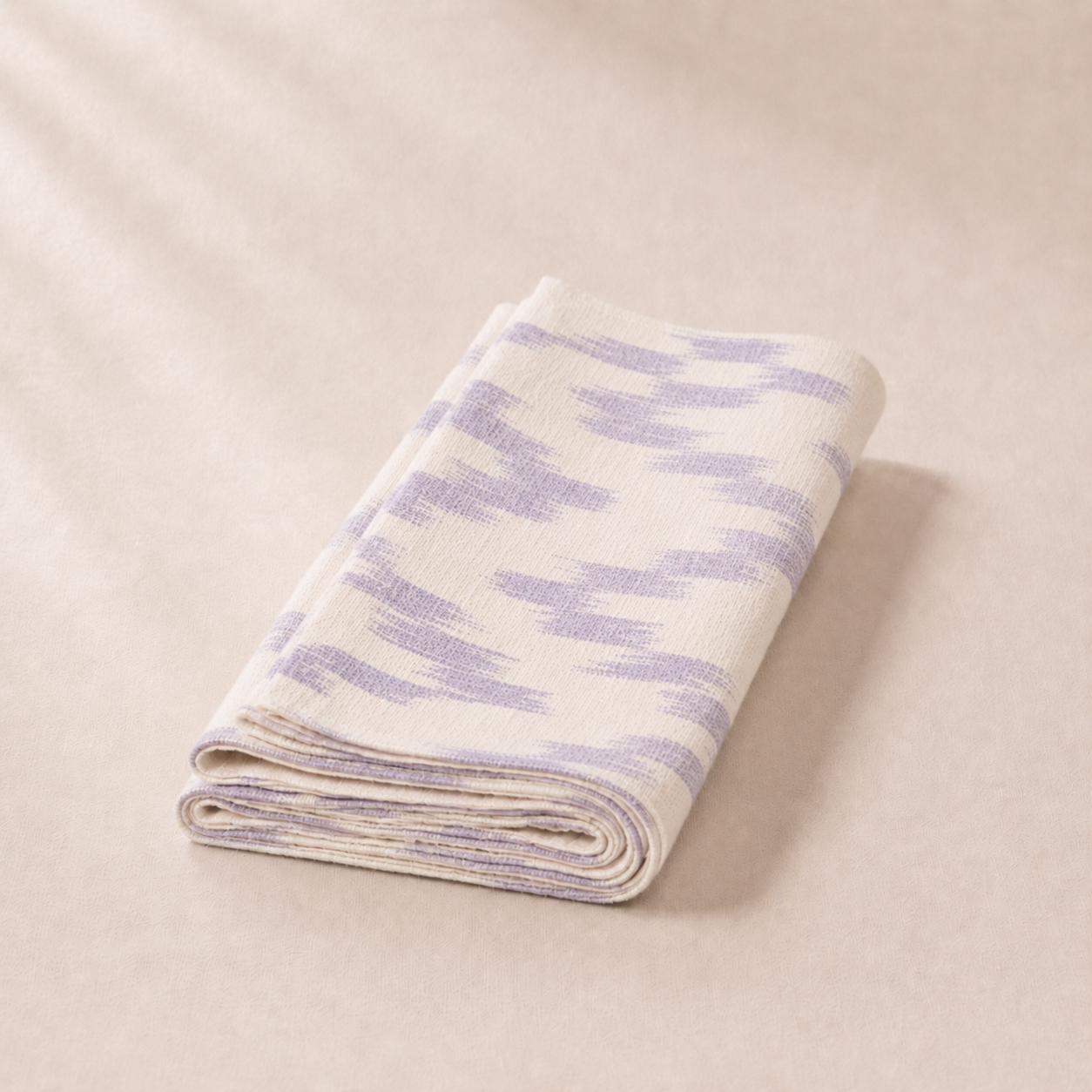 Folded blanket with purple and white pattern on a beige background