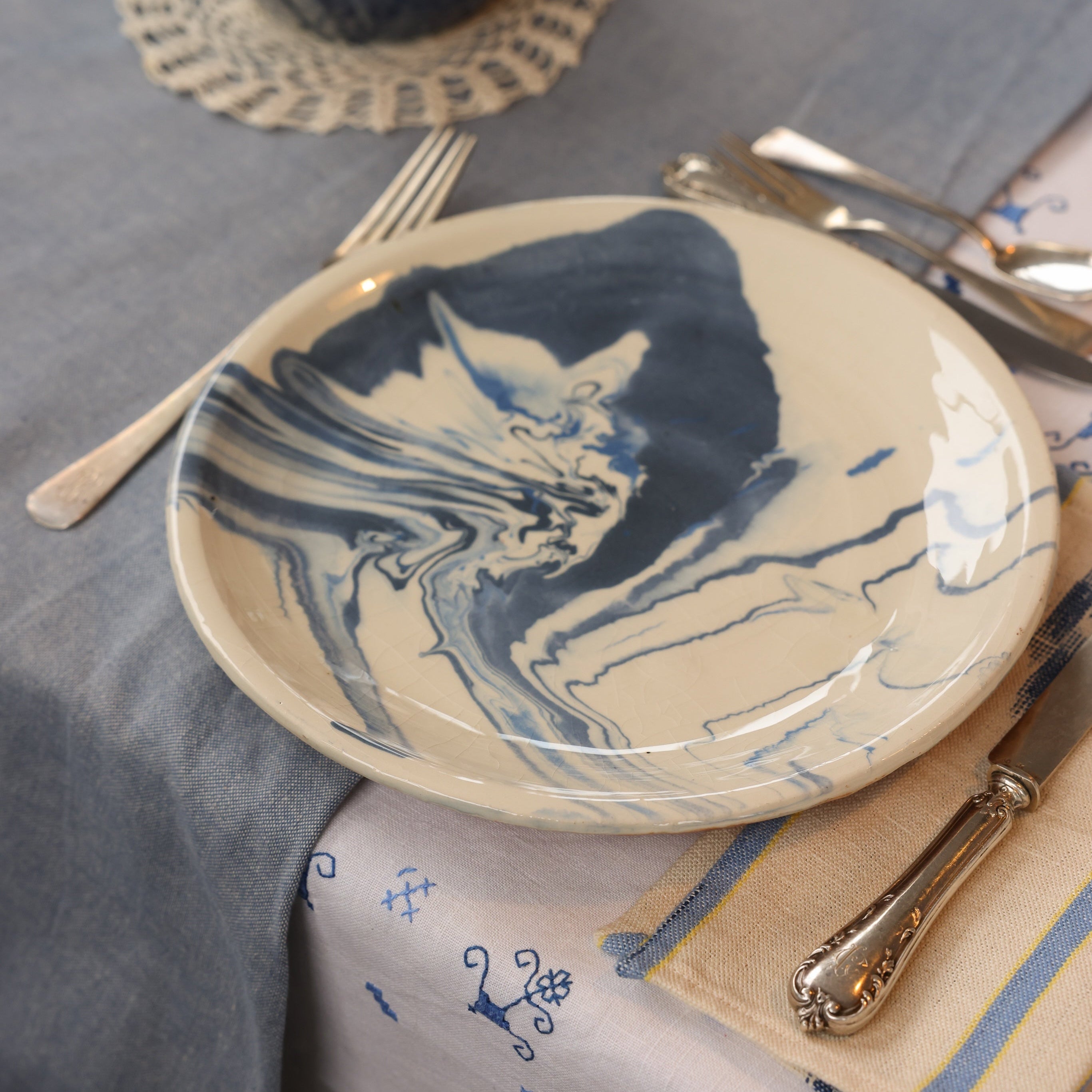 Table setting with a ceramic plate featuring blue abstract design on a gray tablecloth.