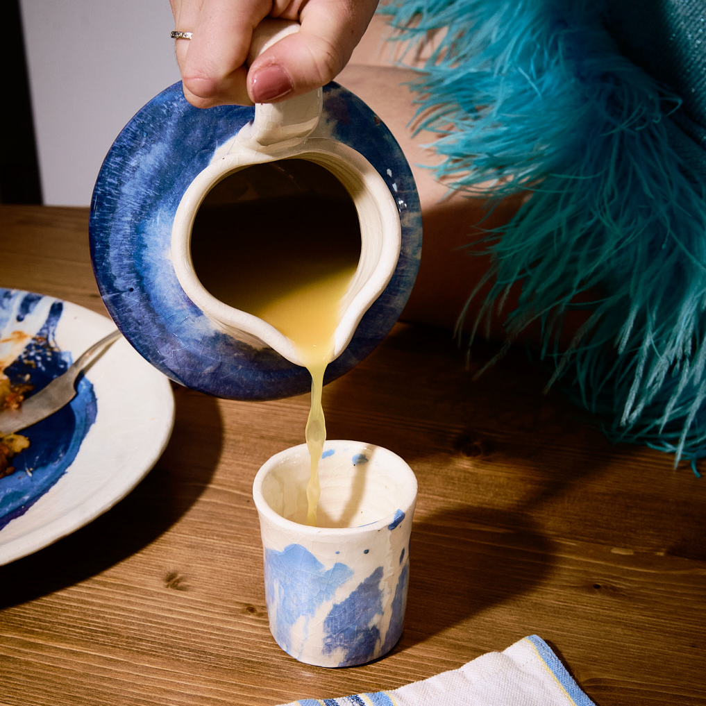 Person pouring liquid from a blue and white pitcher into a matching cup on a wooden table. - lifestyle