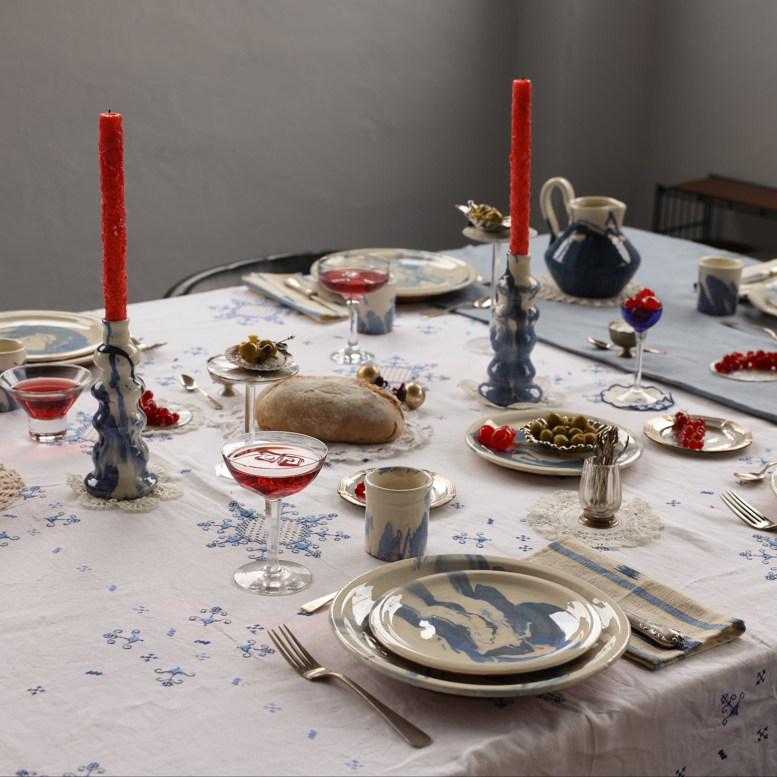 Elegant dinner table setting with red candles, blue and white crockery, and floral tablecloth.