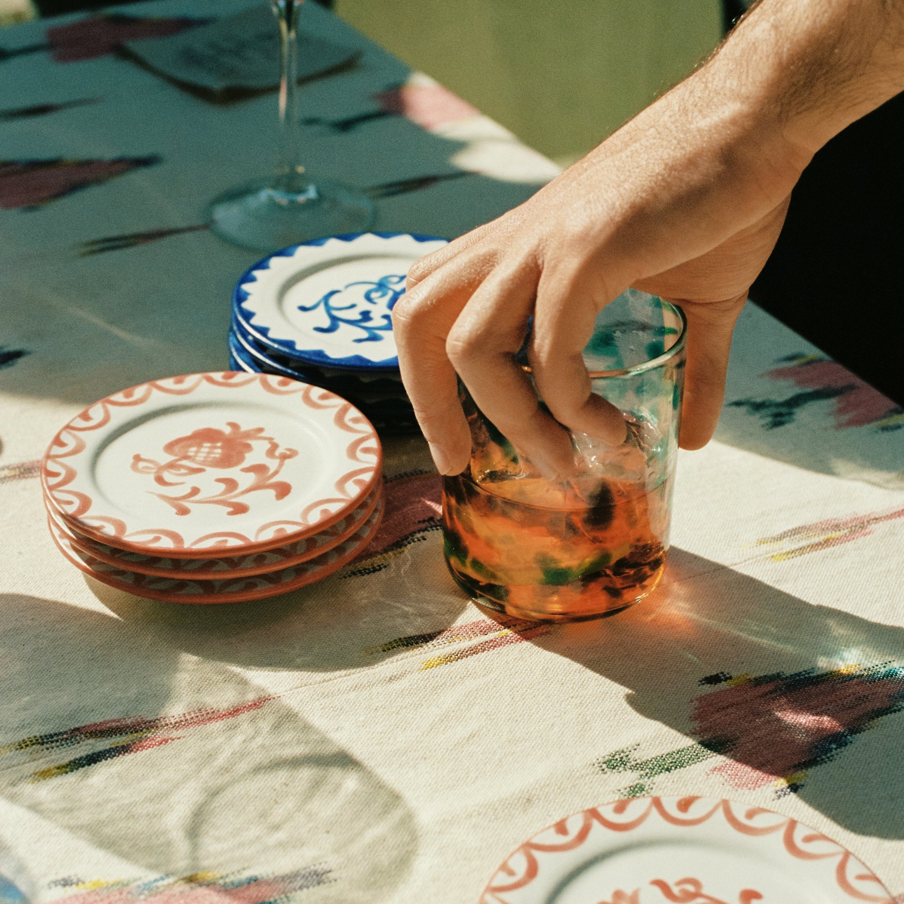 Hand holding a glass of iced tea on a patterned tablecloth with plates in the background - lifestyle