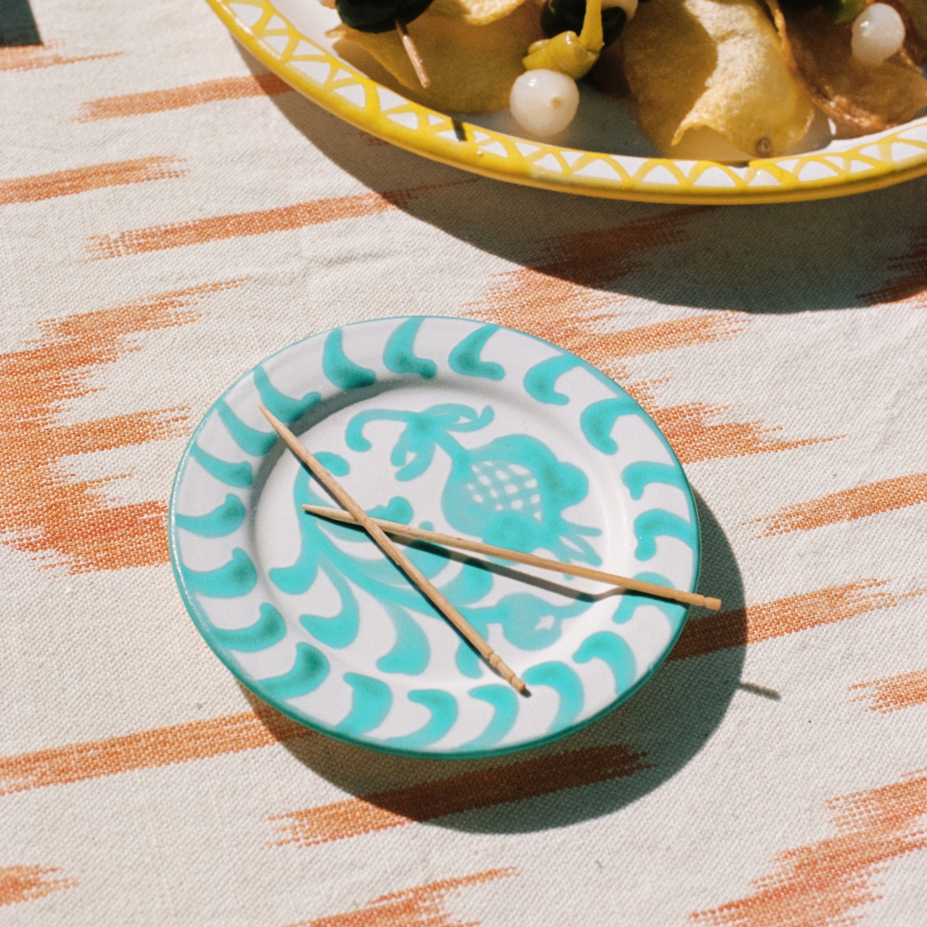 Teal and white decorative plate with toothpicks on a patterned tablecloth