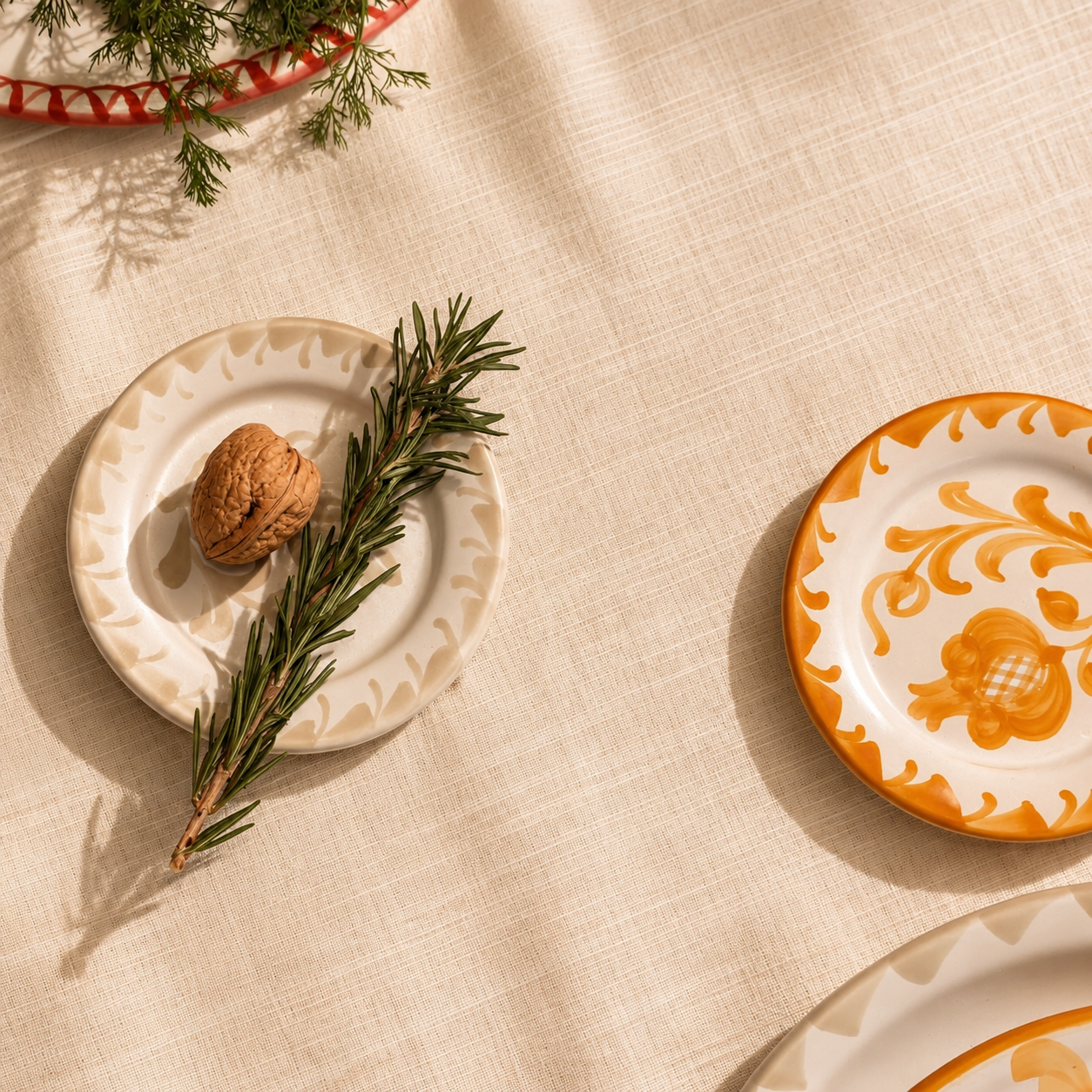 A styled flat-lay of ceramic plates on a textured beige linen tablecloth, decorated with a walnut and a sprig of rosemary. - lifestyle
