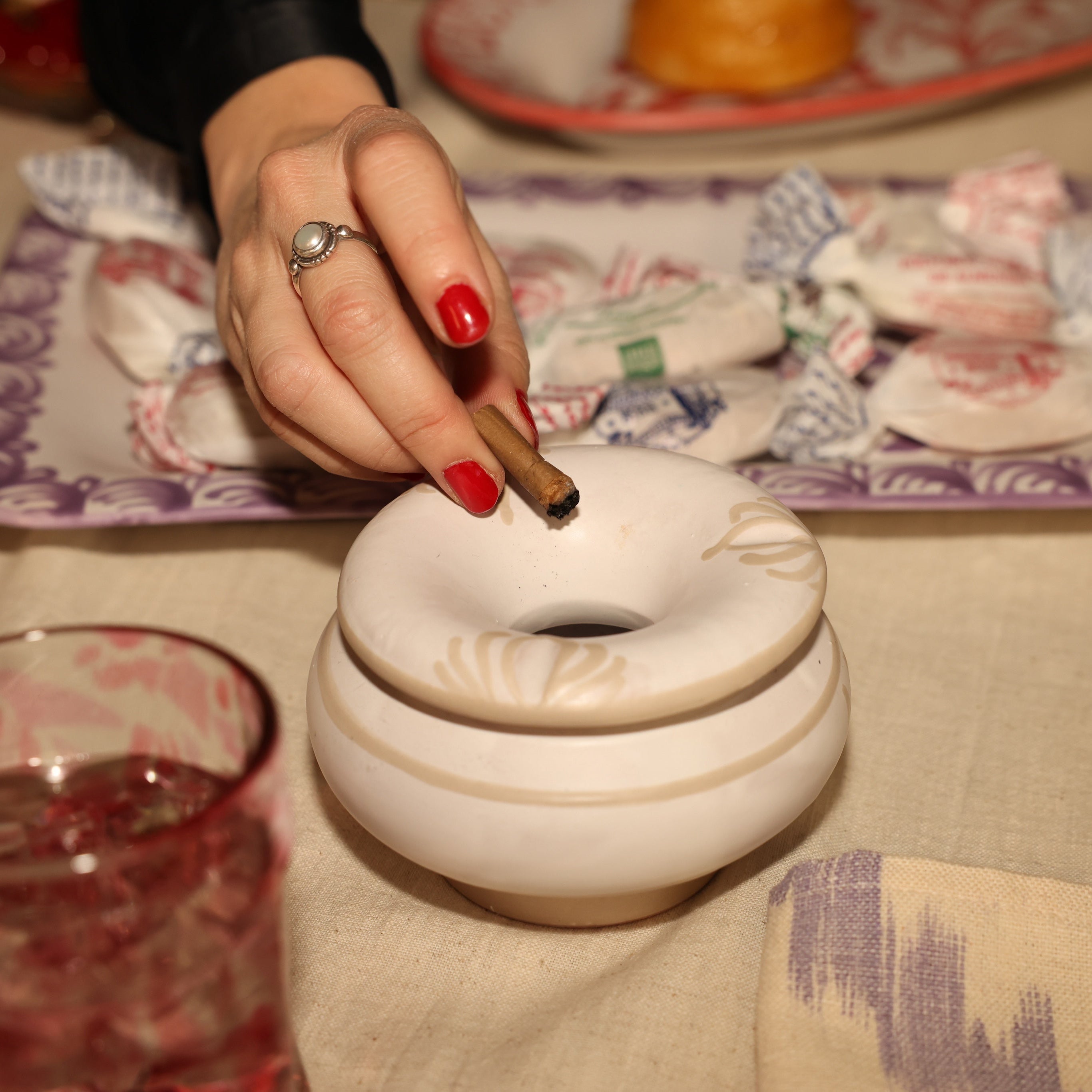 Person lighting a cigarette from an ornate white lighter on a patterned tablecloth. - lifestyle