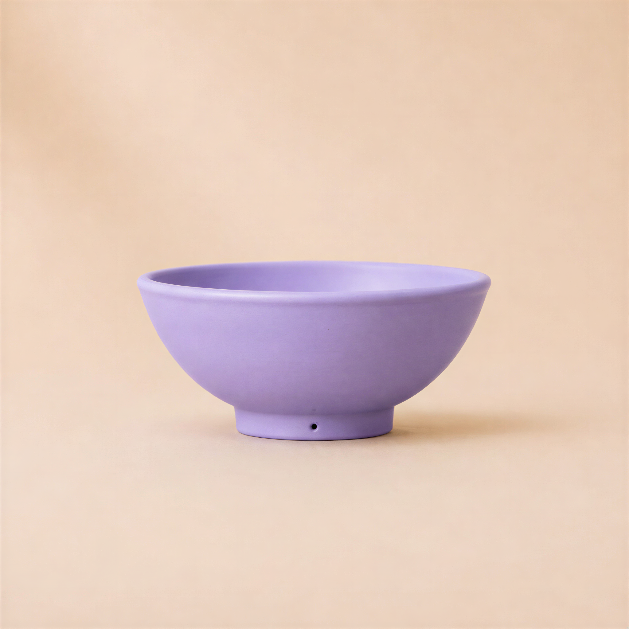 A small lilac ceramic bowl with a short pedestal base, photographed against a solid beige background.