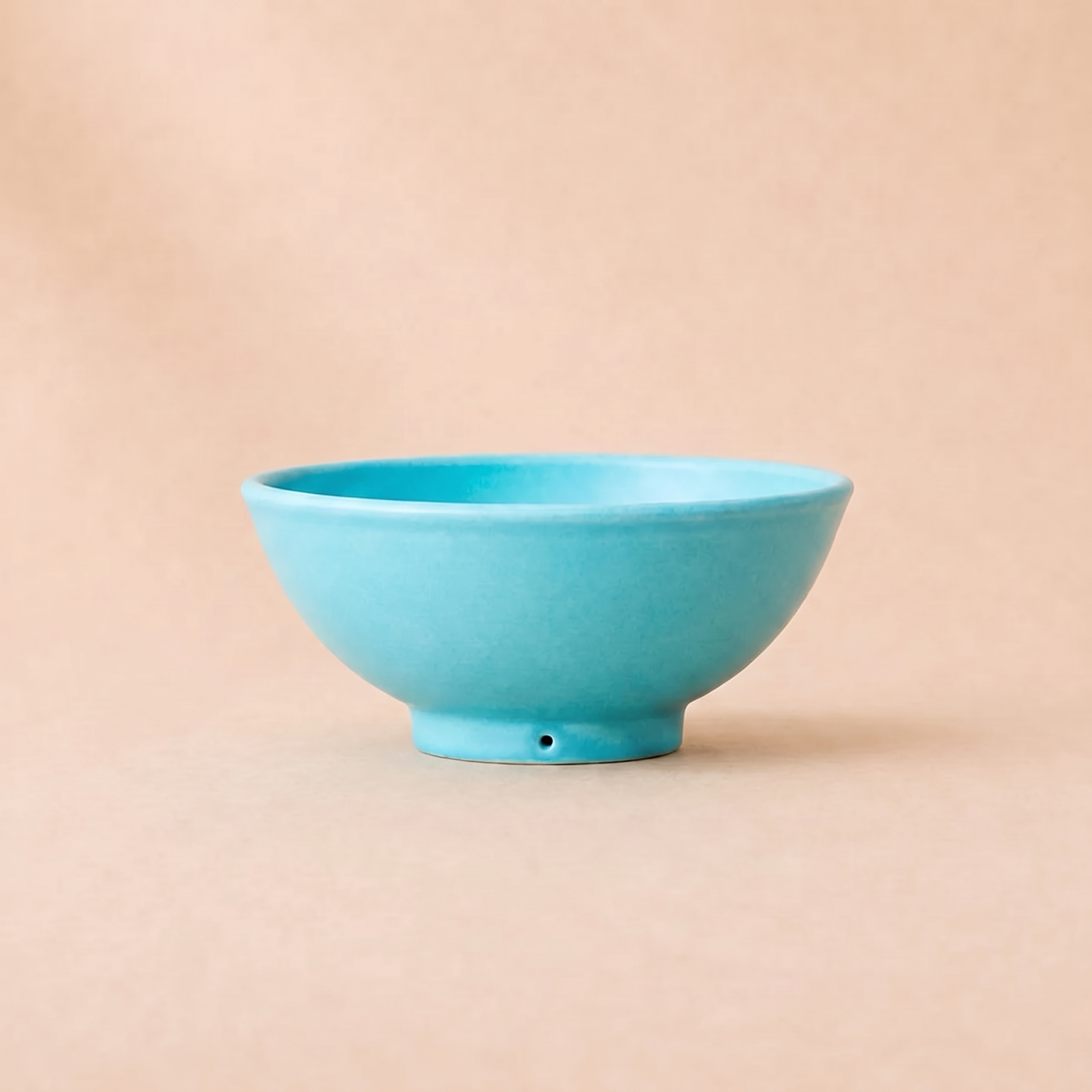 A small turquoise ceramic bowl with a short pedestal base, photographed against a solid beige background.