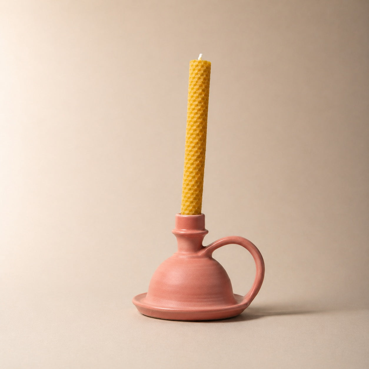 Yellow candle in a pink ceramic holder on a beige background