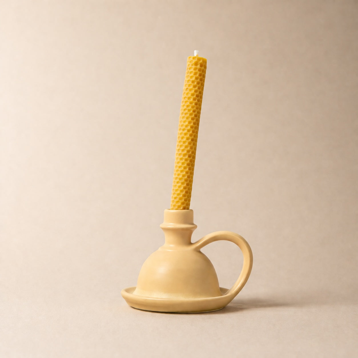 Beige candle holder with a yellow candle on a beige background