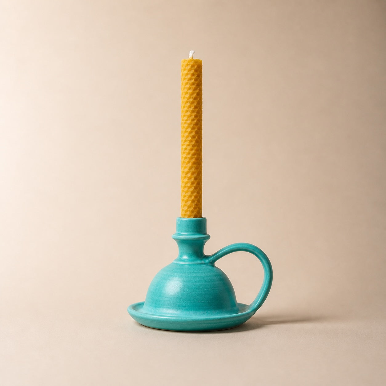 Turquoise candle holder with a yellow candle on a beige background
